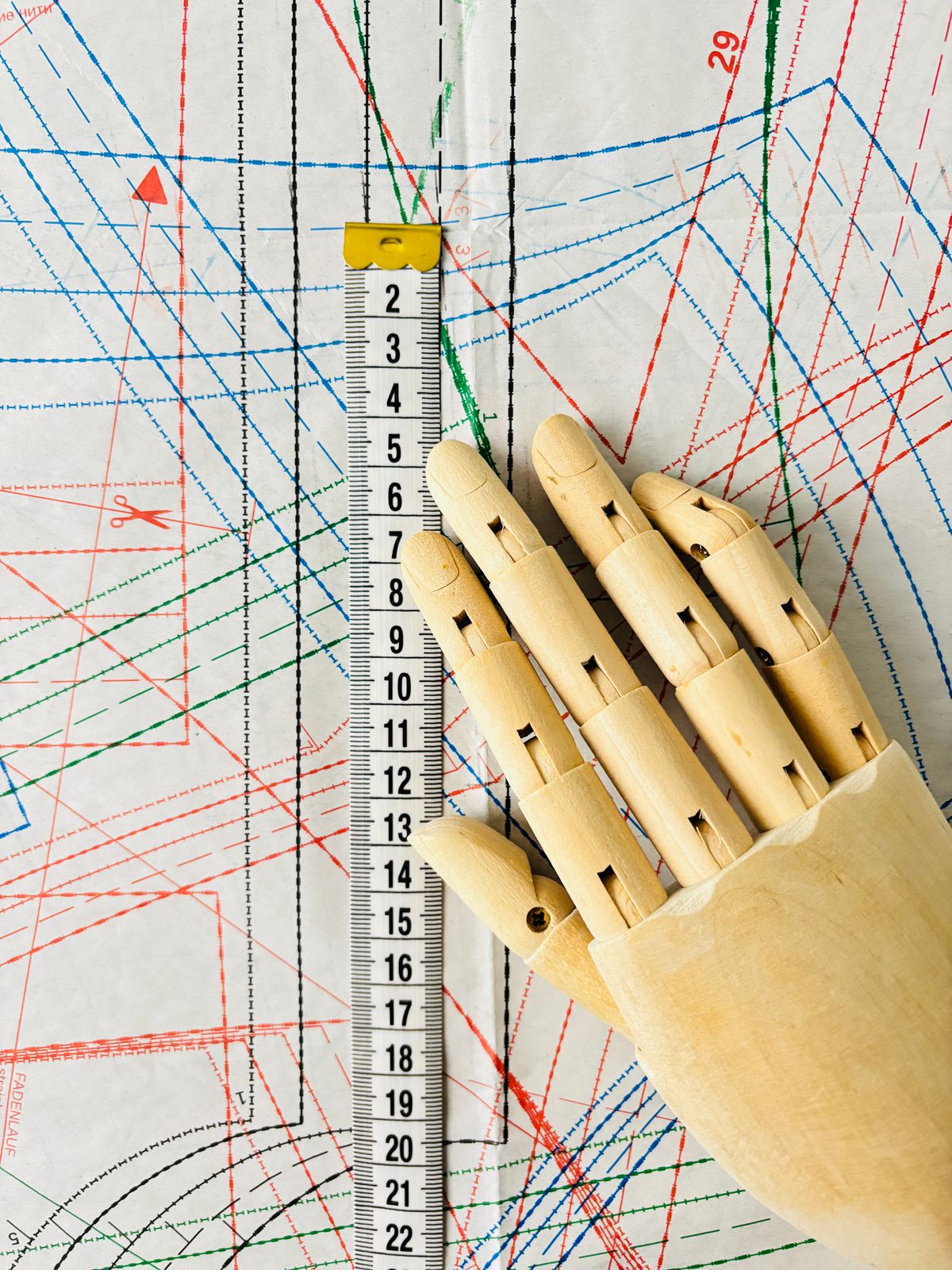 Wooden mannequin hand resting on paper sewing patterns with a measuring tape