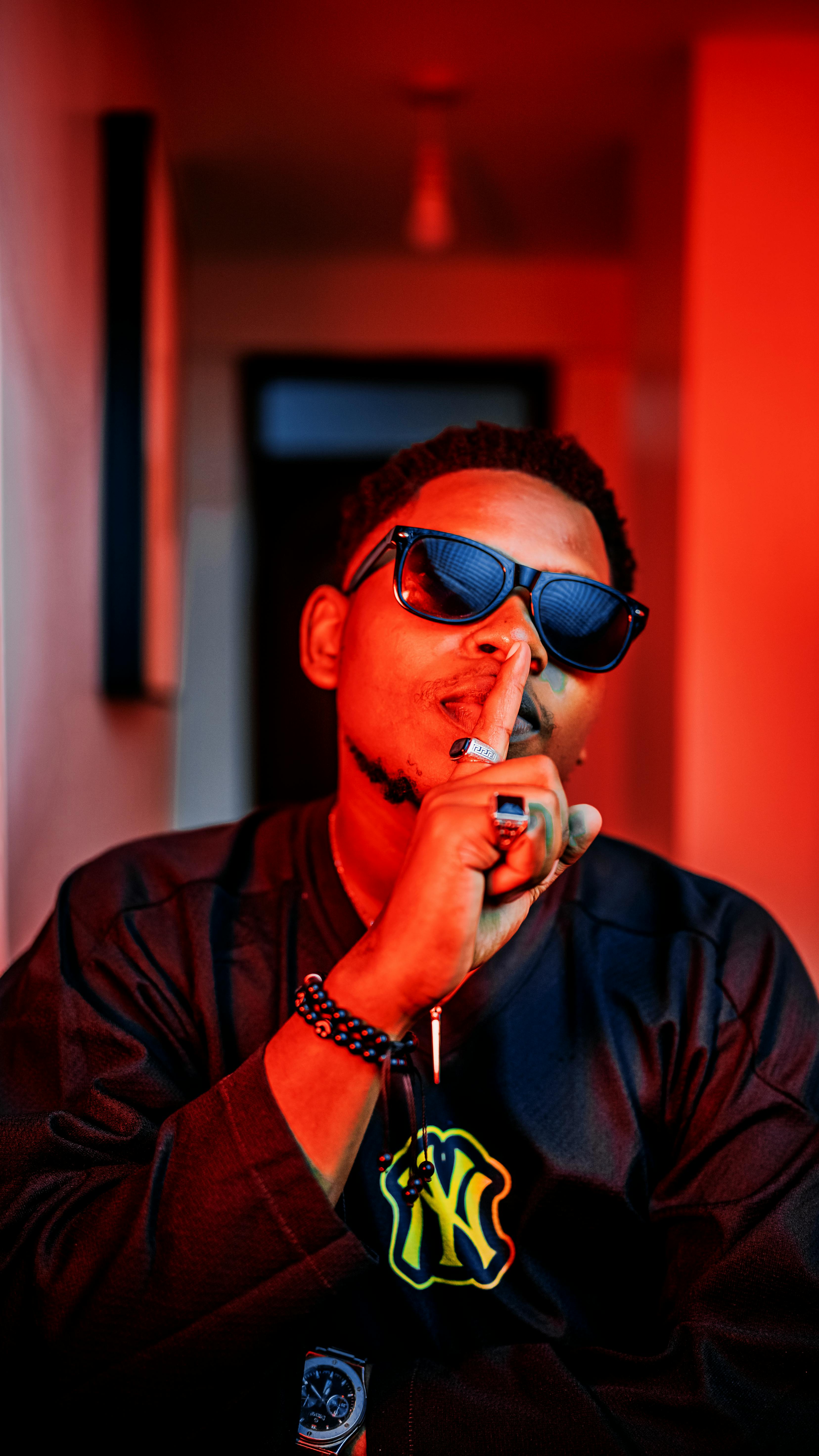 A fashionable man making a shushing gesture with bold red lighting indoors.