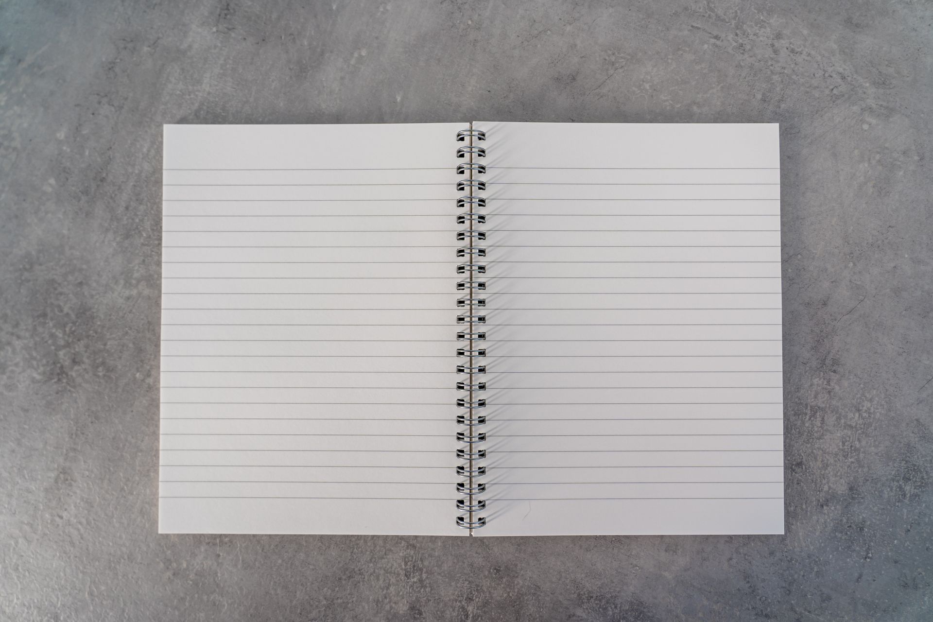 Top-down view of an open spiral notebook with lined pages on a textured gray surface.
