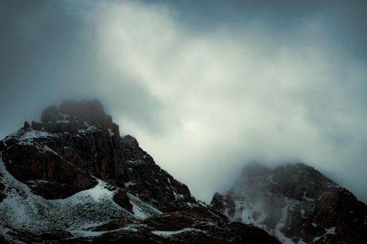 A dramatic view of snow-covered mountain peaks enveloped in mist, creating a moody and mysterious atmosphere.
