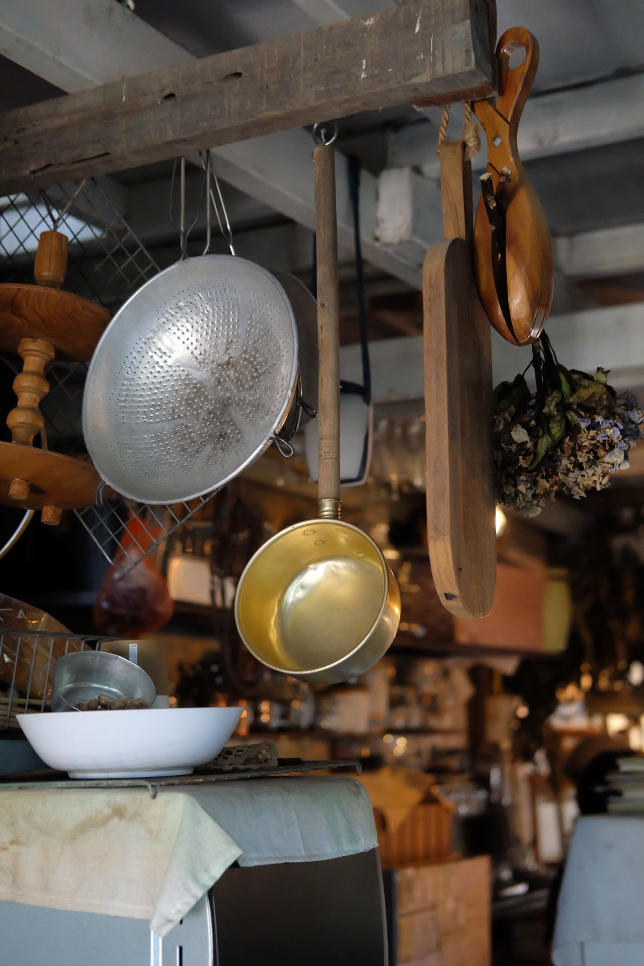 Copper pan, metal colander and wooden cutting boards hanging from hooks on a rustic wooden beam