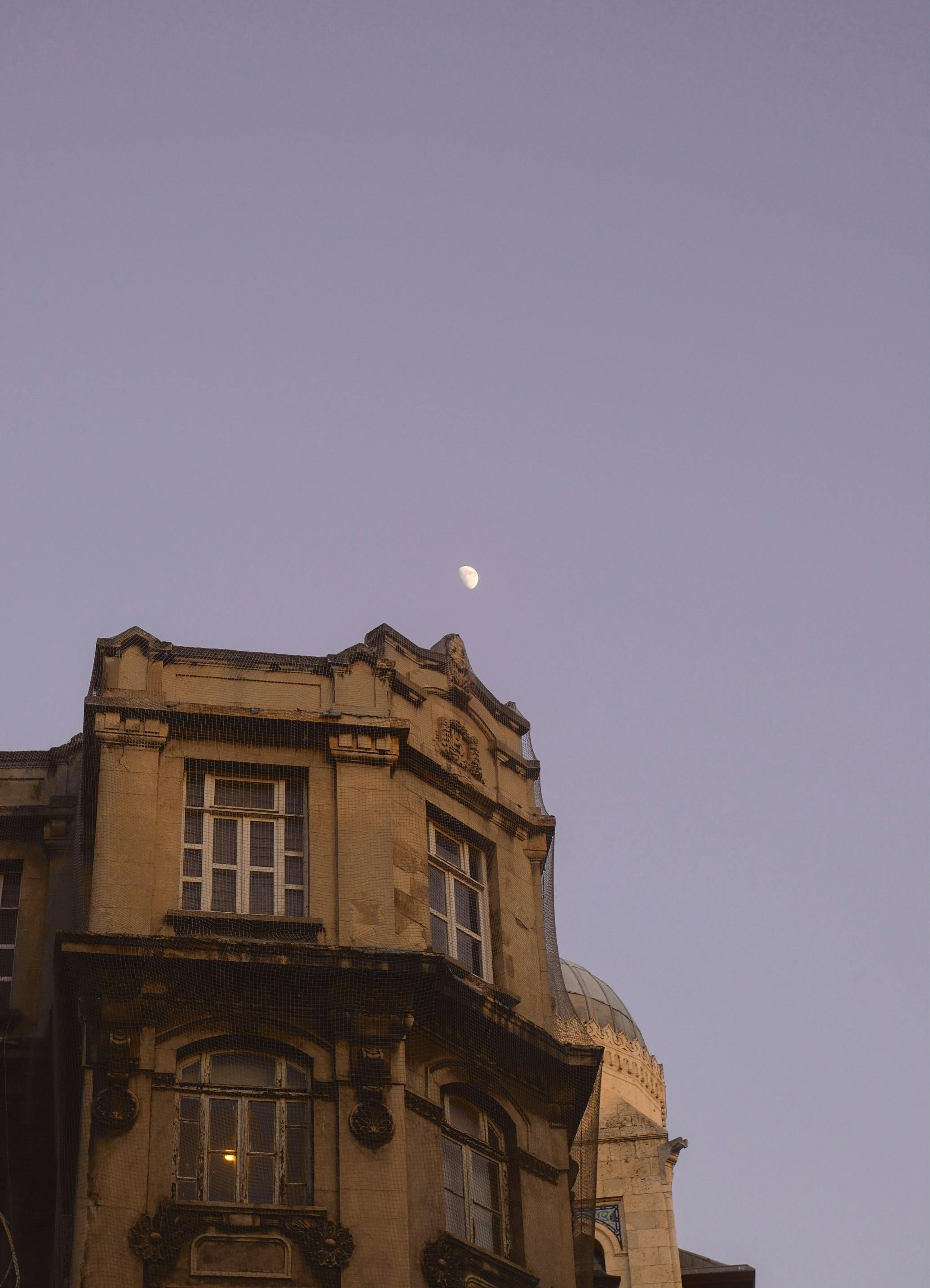 grátis A fachada de um prédio clássico, com a lua em um céu claro ao entardecer, exala um charme vintage. Foto profissional