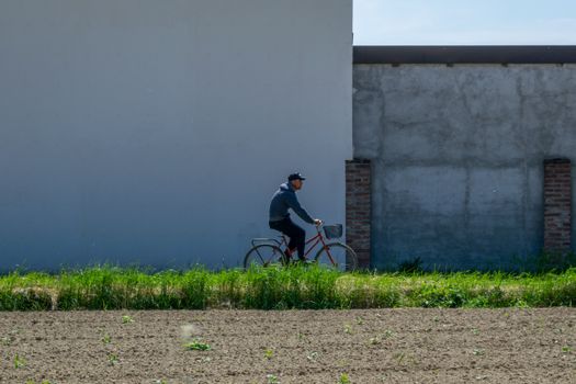 A cyclist in Piamonte, Italy rides past a rustic wall in a rural setting, capturing the essence of Italian countryside life.