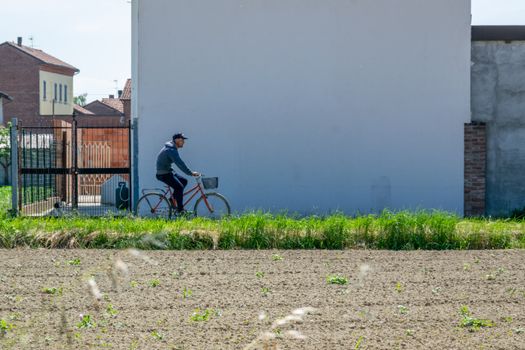 A person cycling on a rural road in Castellazzo Bormida, Italy, with farmland and buildings in the background.