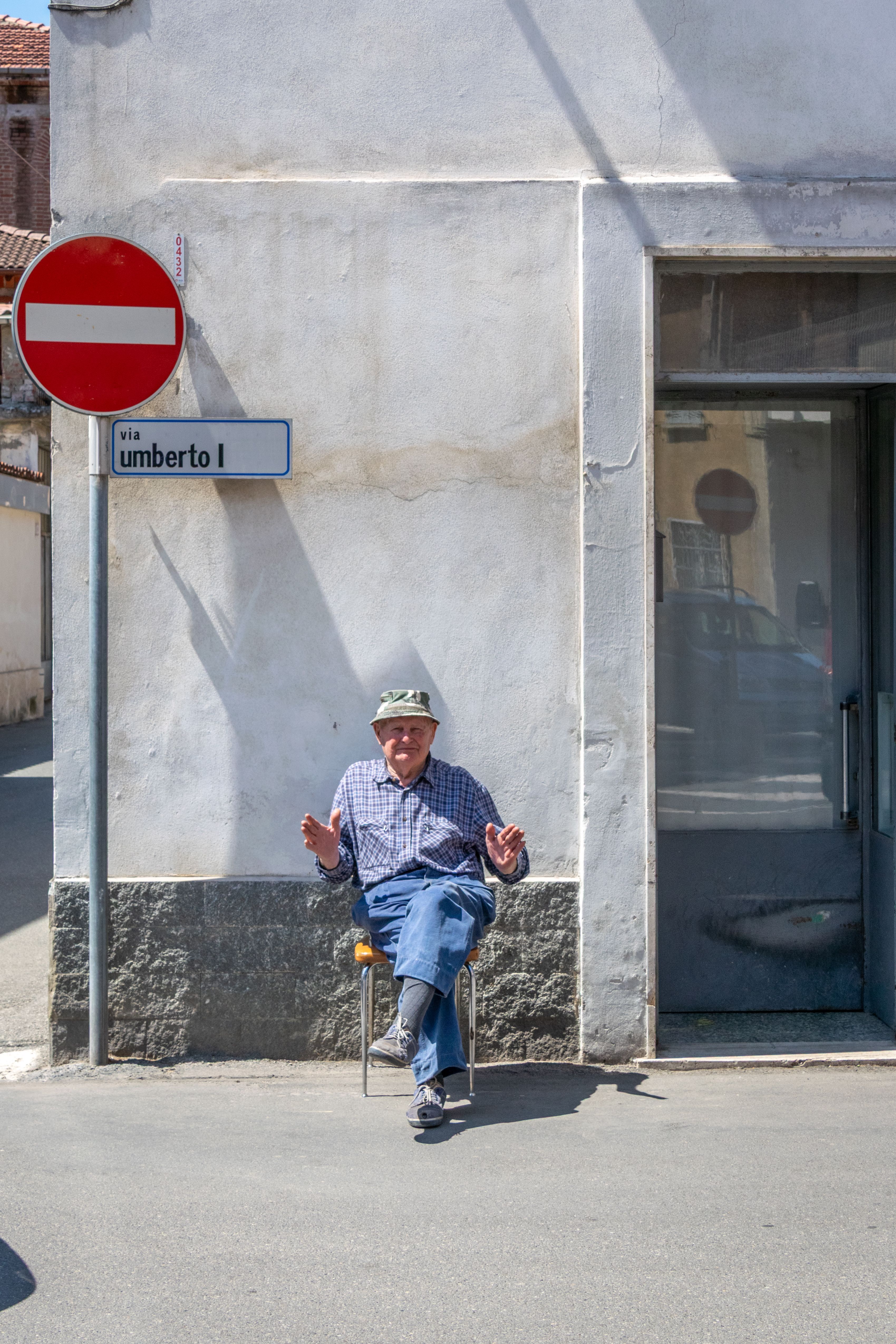 Senior man sitting with shadows on Via Umberto I in Castellazzo Bormida, Italy on a sunny day.