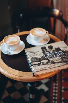Cozy café table scene with cappuccinos and Russian book on Notre-Dame, captured indoors.