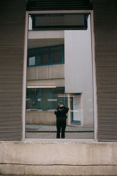Free A photographer's reflection in a building window in Hasselt, Belgium captures urban architecture. Stock Photo