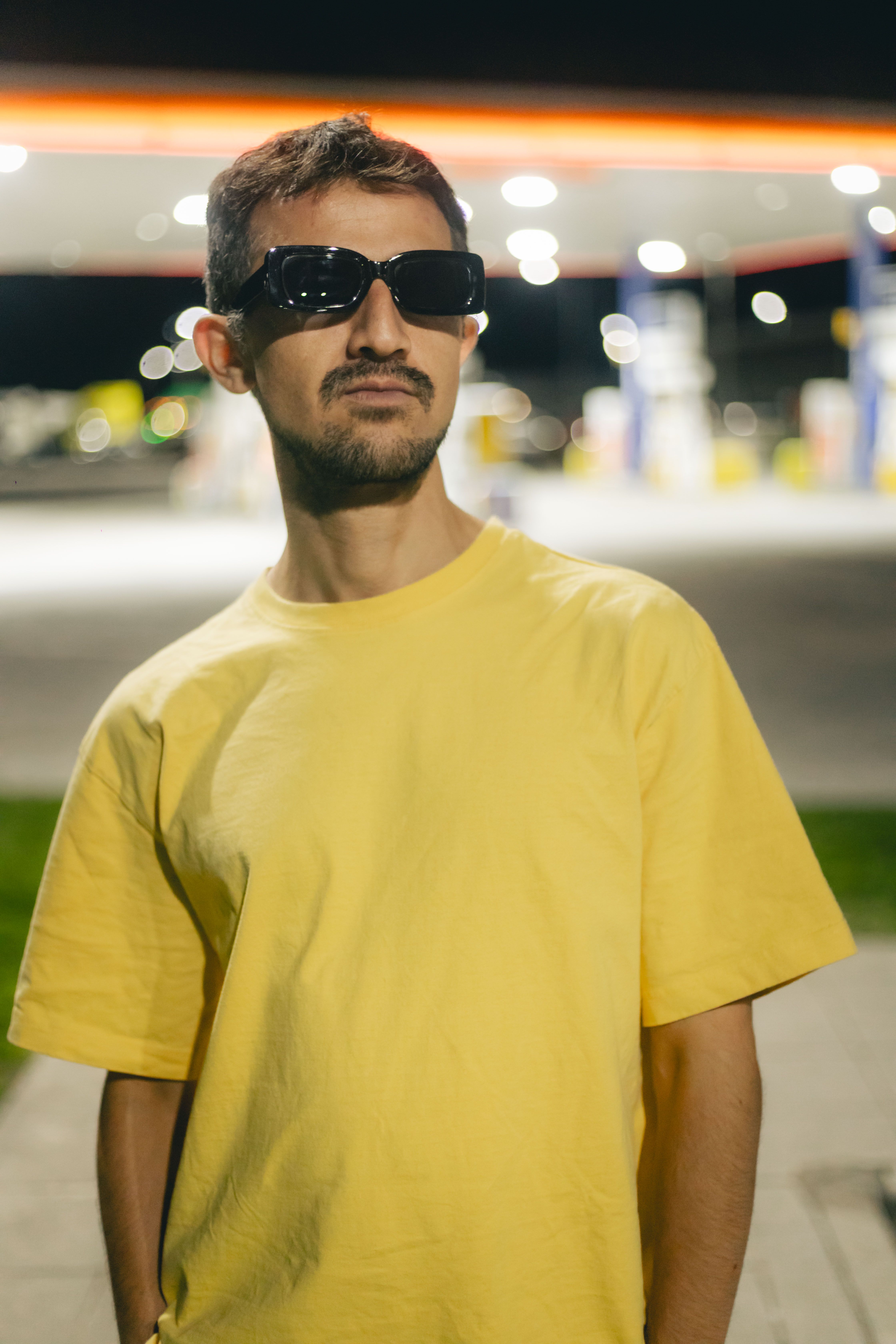 Man in sunglasses and yellow shirt at a modern gas station during night.