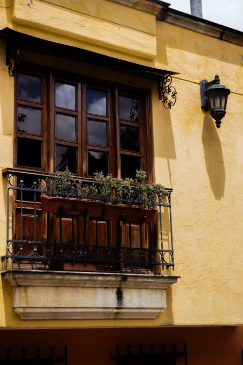 Free Charming rustic balcony with flower pots on a vibrant yellow wall, bathed in daylight. Stock Photo
