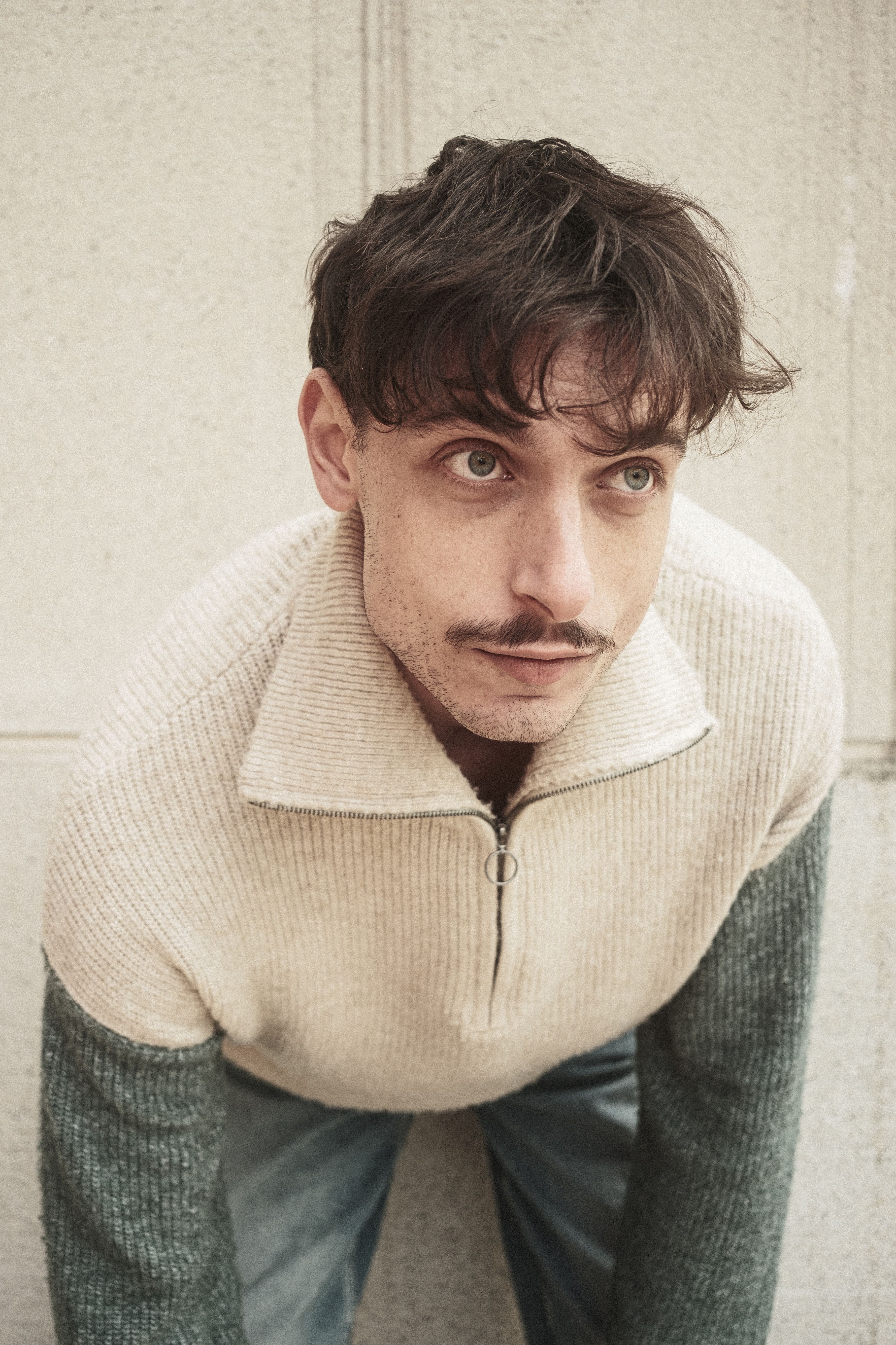 Casual portrait of a young man with a mustache wearing a zip-up sweater.