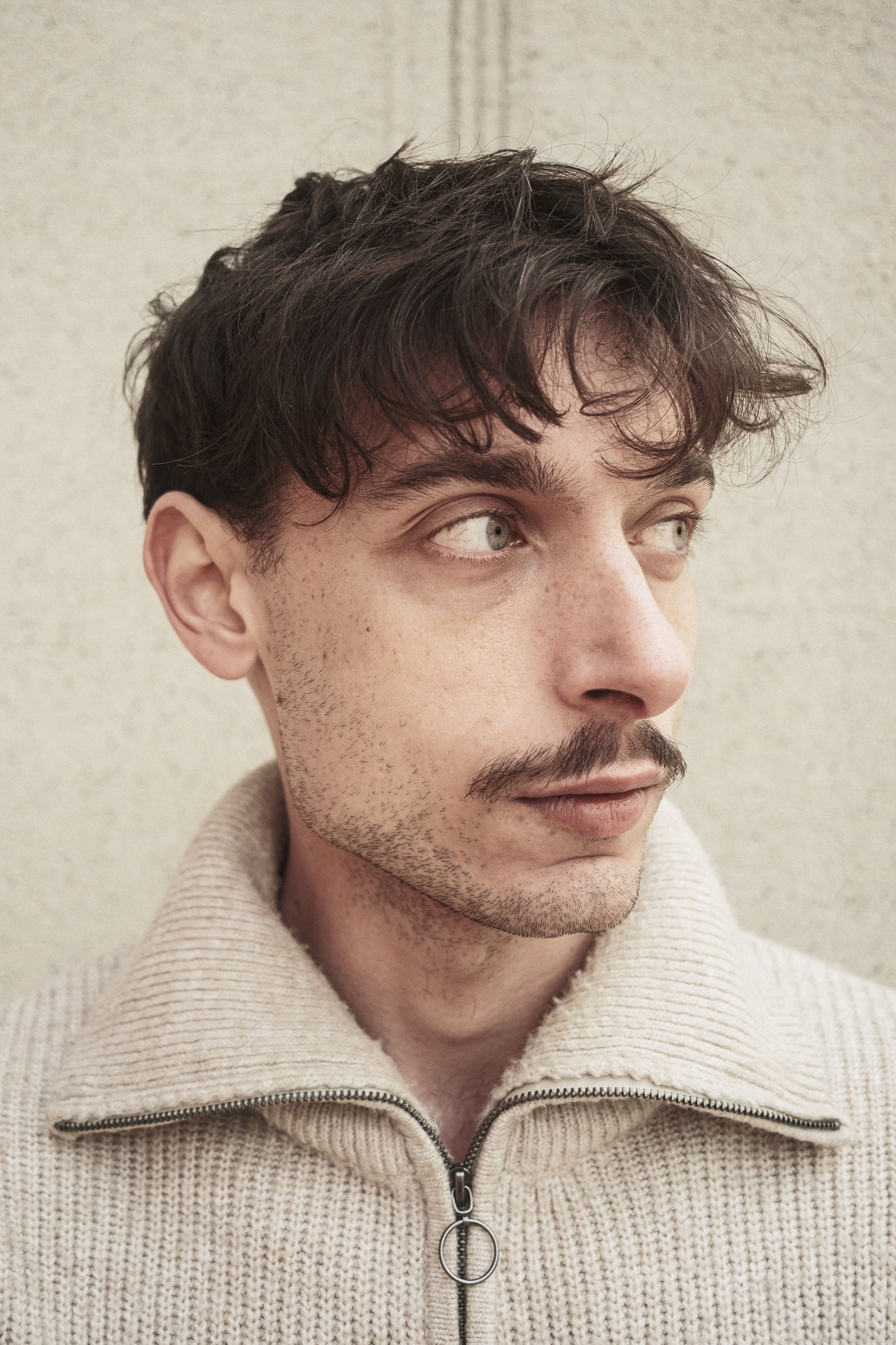 Stylish young man with mustache in cozy beige sweater, looking away.