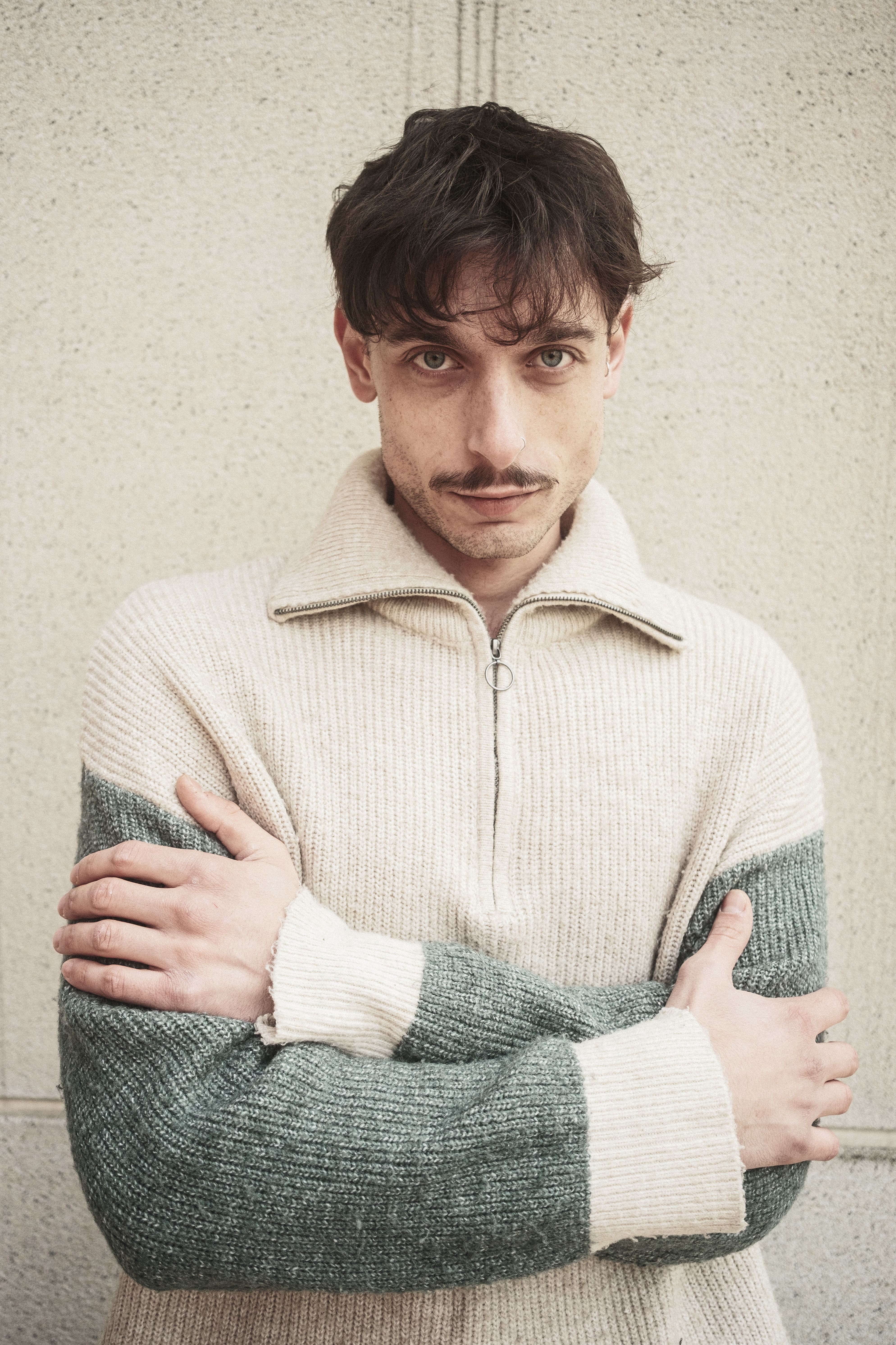 A man in a cozy knit sweater stands against a textured wall, exuding warmth and style.