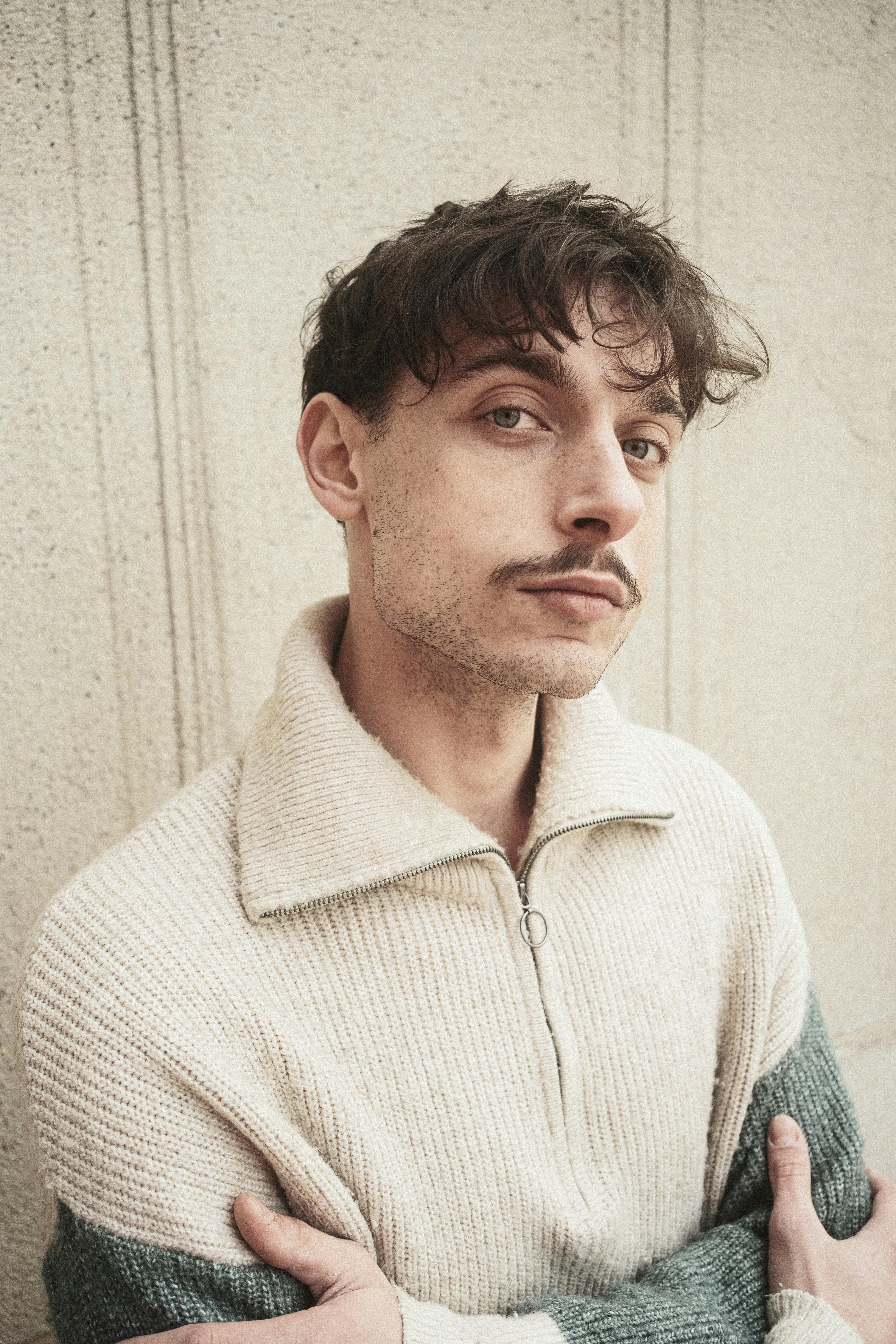 Stylish young man with mustache posing confidently against a textured background.