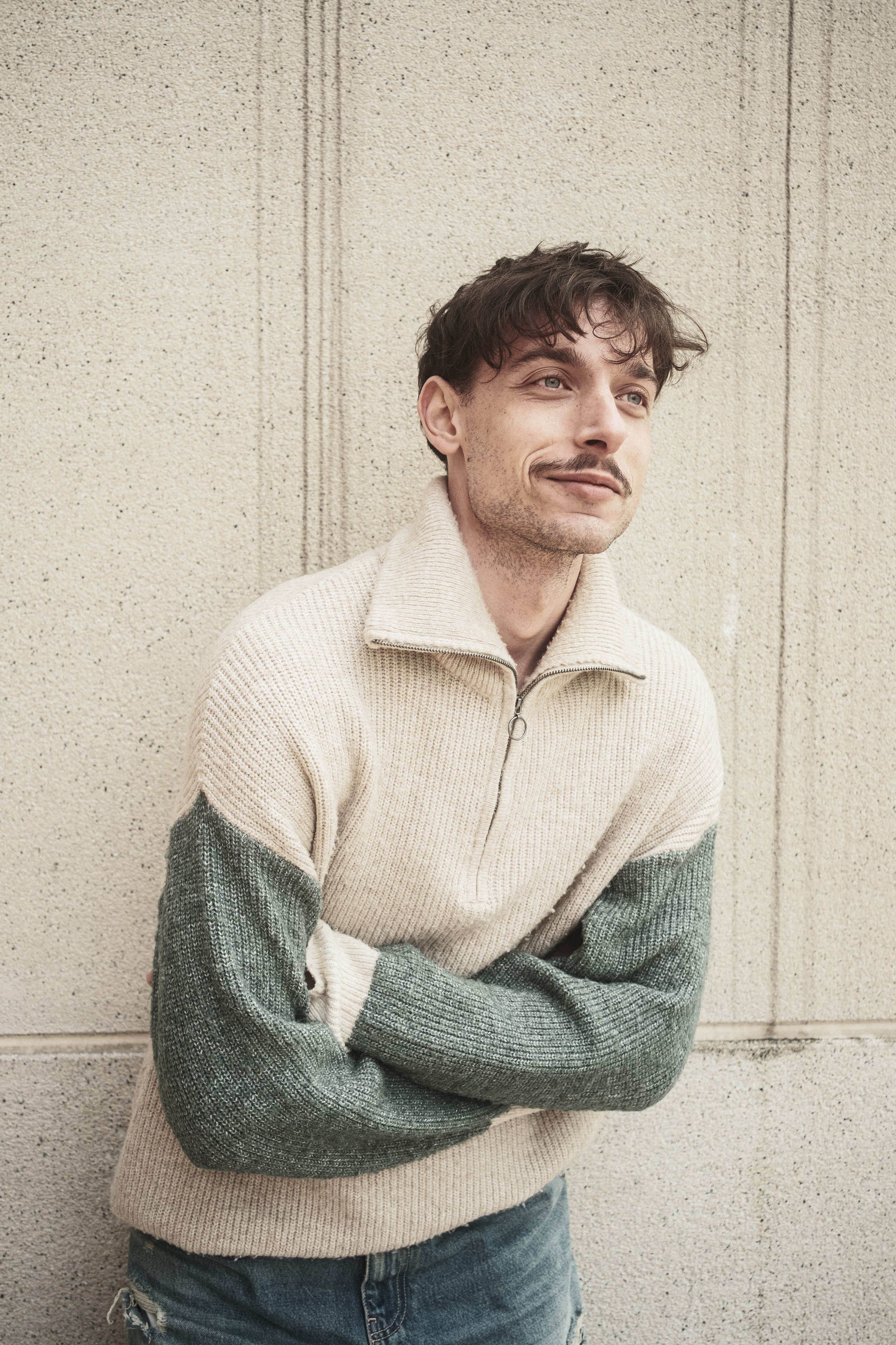 Stylish young man in cozy sweater leaning against a textured wall.