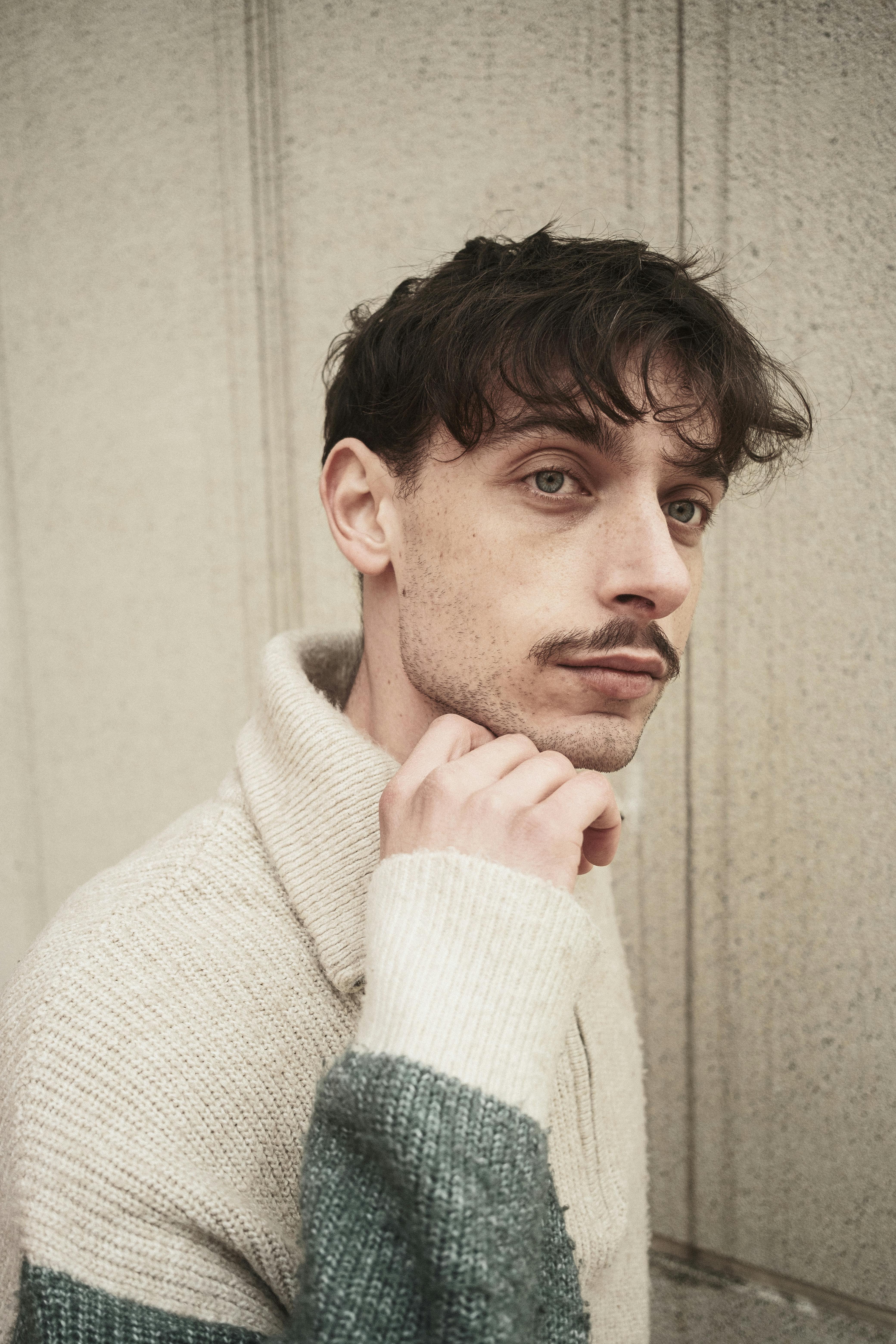 Side profile of a man in a cozy sweater against a textured wall, exuding a thoughtful vibe.