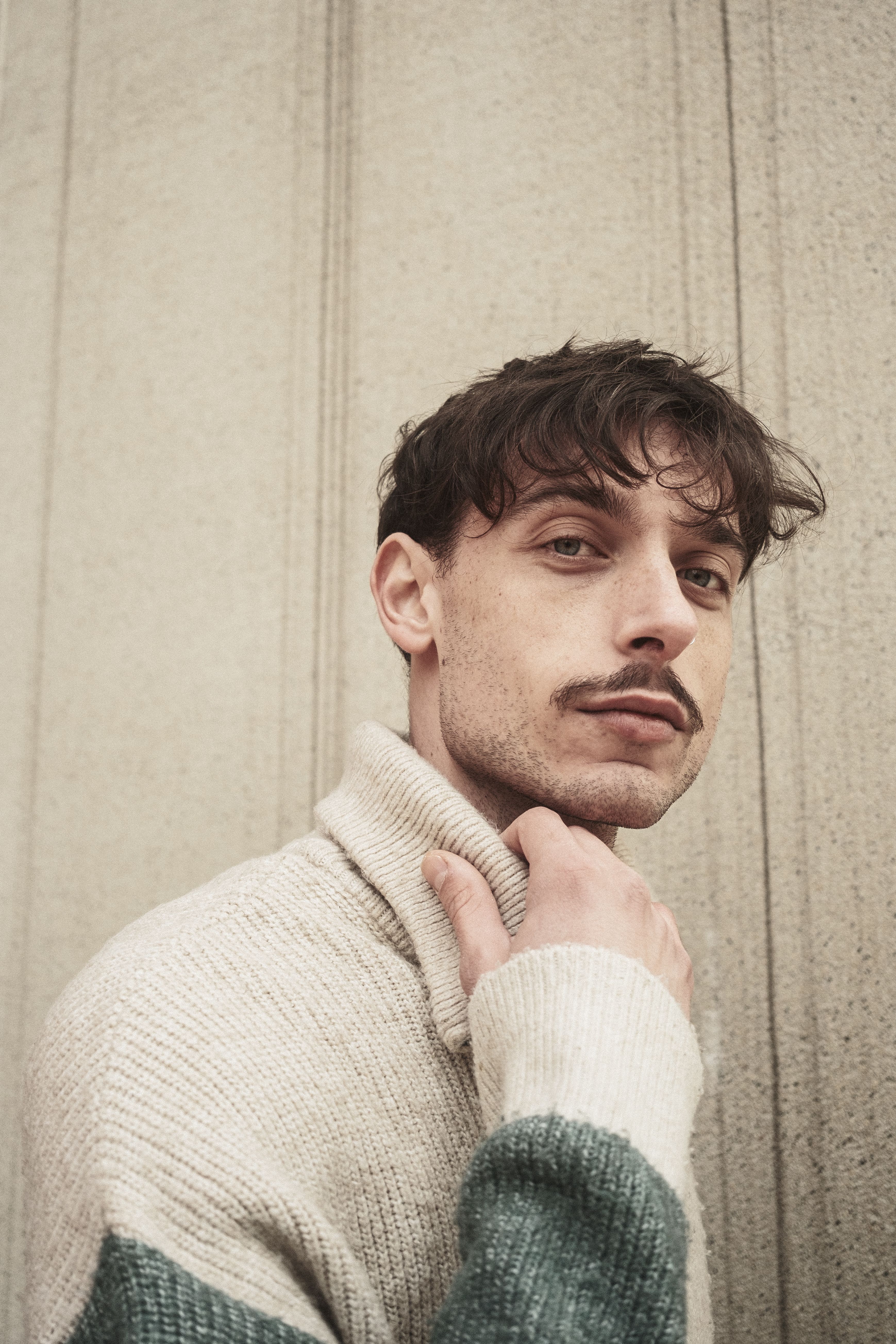 Portrait of a trendy man in a wool sweater posing against a textured wall.