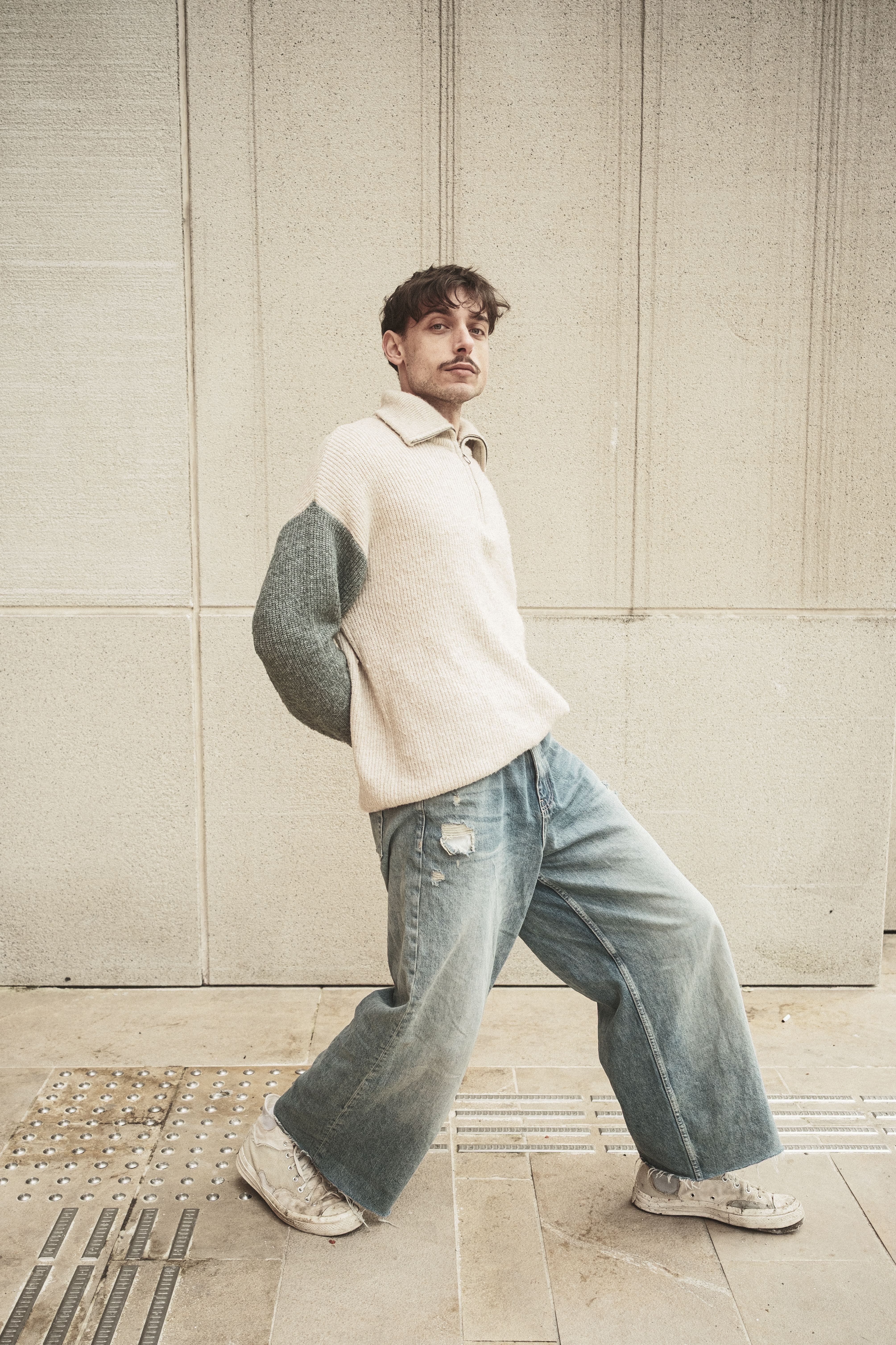 Young man in stylish casual outfit posing against urban backdrop.