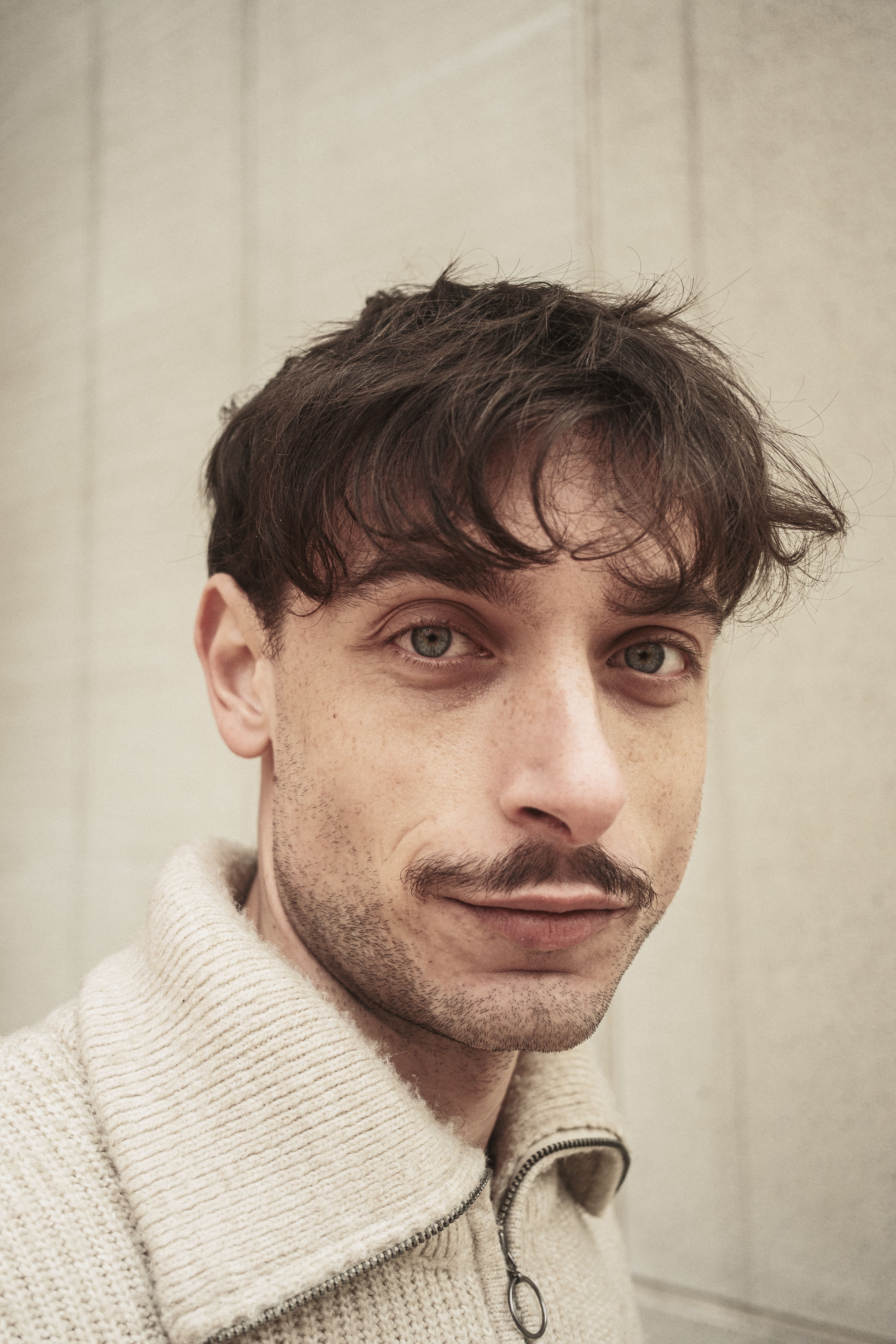 Close-up portrait of a young man with dark hair and mustache against a neutral background.