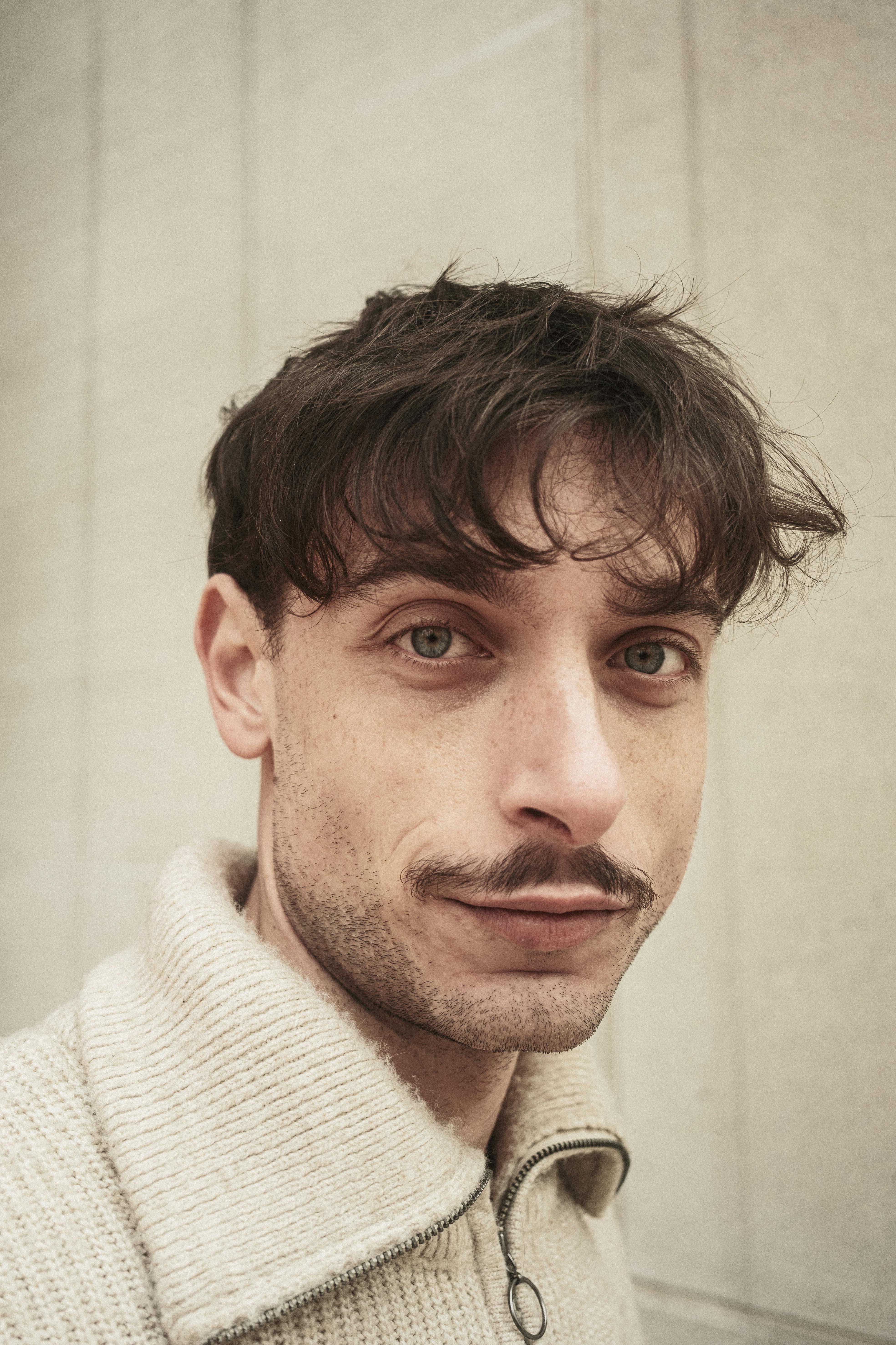Gratuit Portrait en gros plan d'un jeune homme aux cheveux et à la moustache foncés, sur fond neutre. Photos