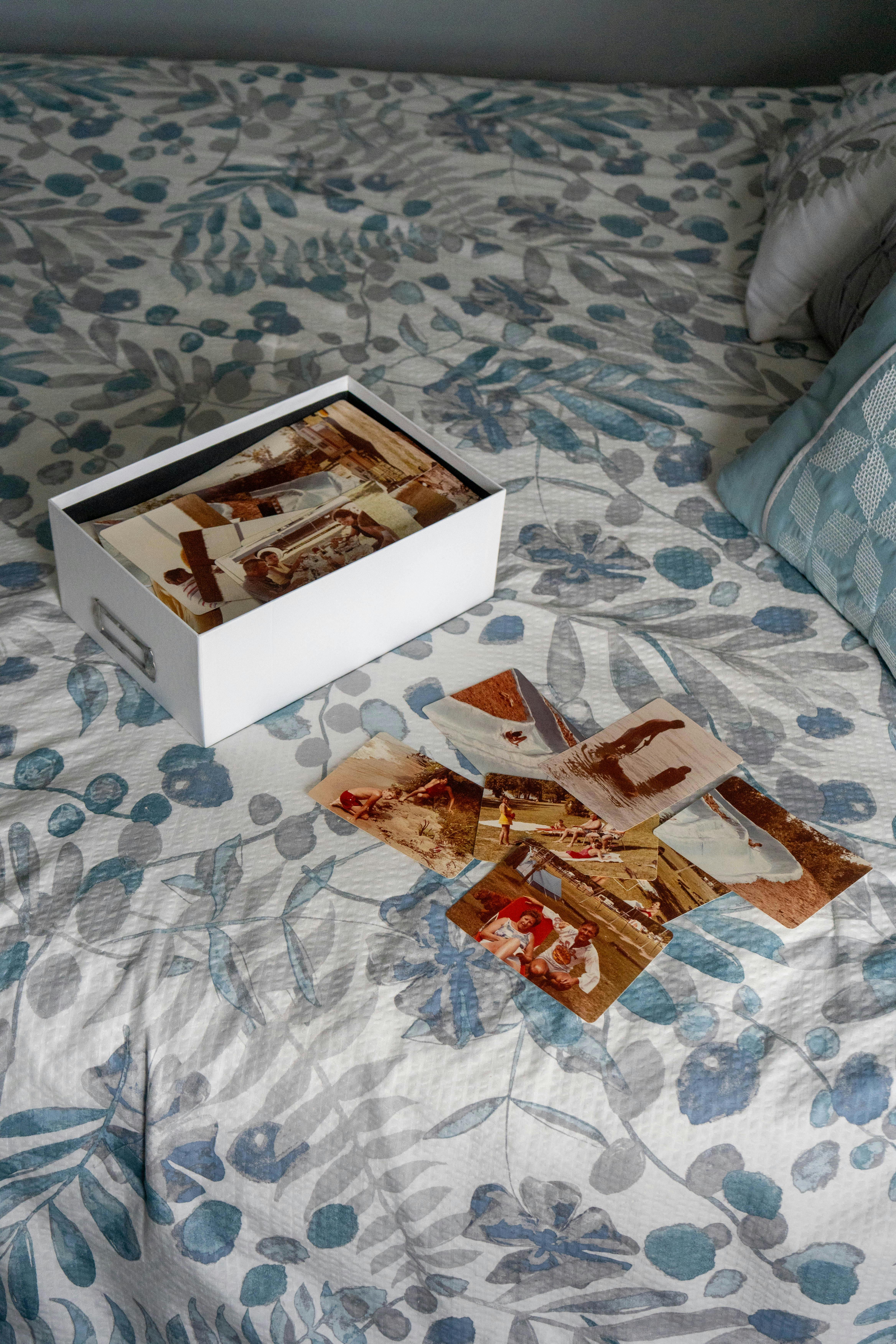 Gratuit Colecție de fotografii de familie nostalgice într-o cutie pe o cuvertură cu motive florale. Fotografie de stoc