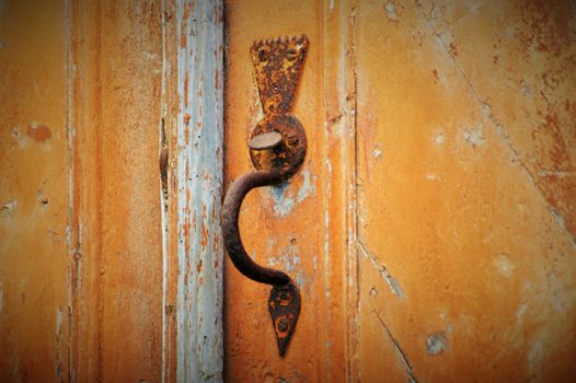 Close-up of a vintage rusty door handle on a weathered wooden door, showcasing rustic charm.