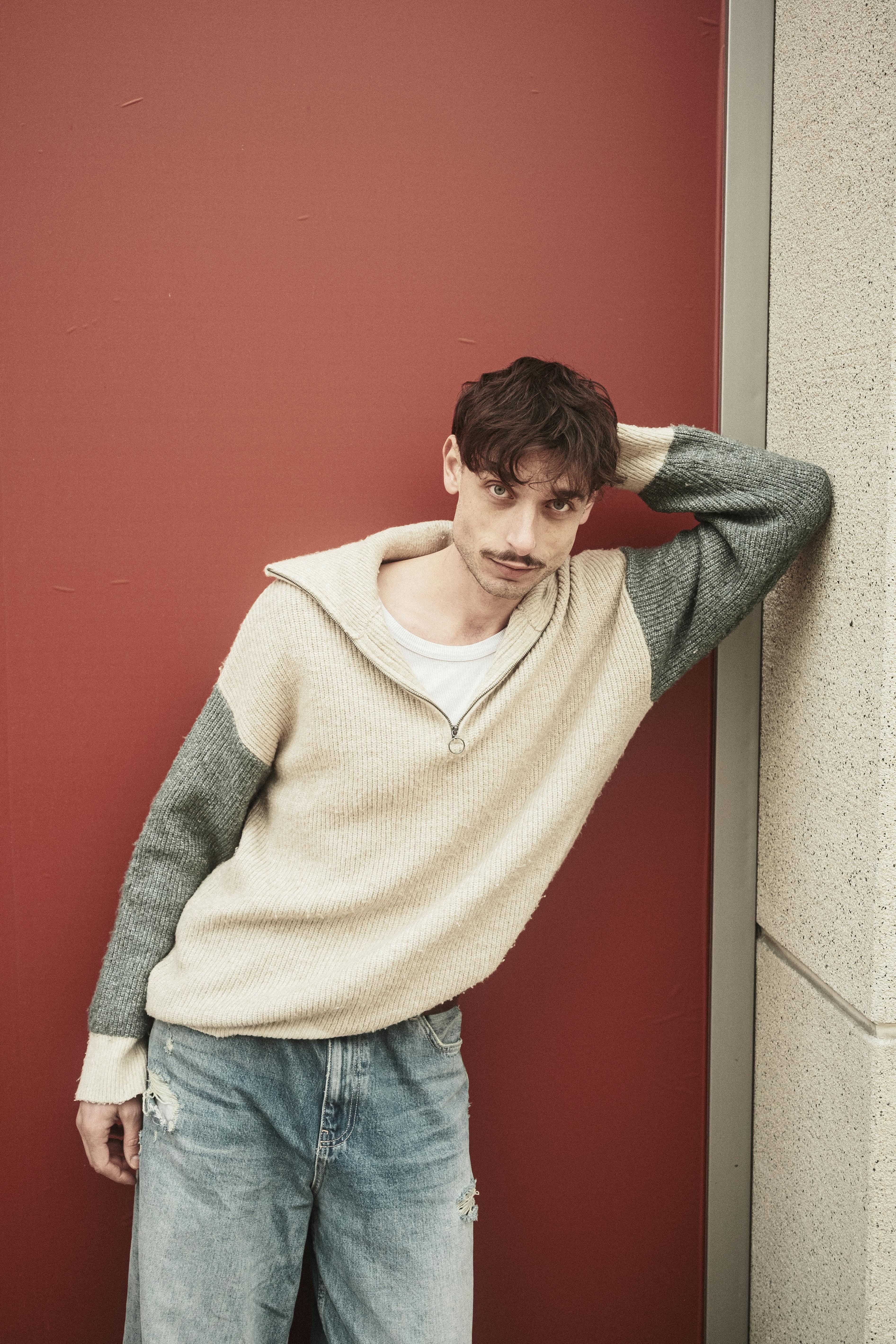 Stylish young man in casual attire leaning against a vibrant red wall.