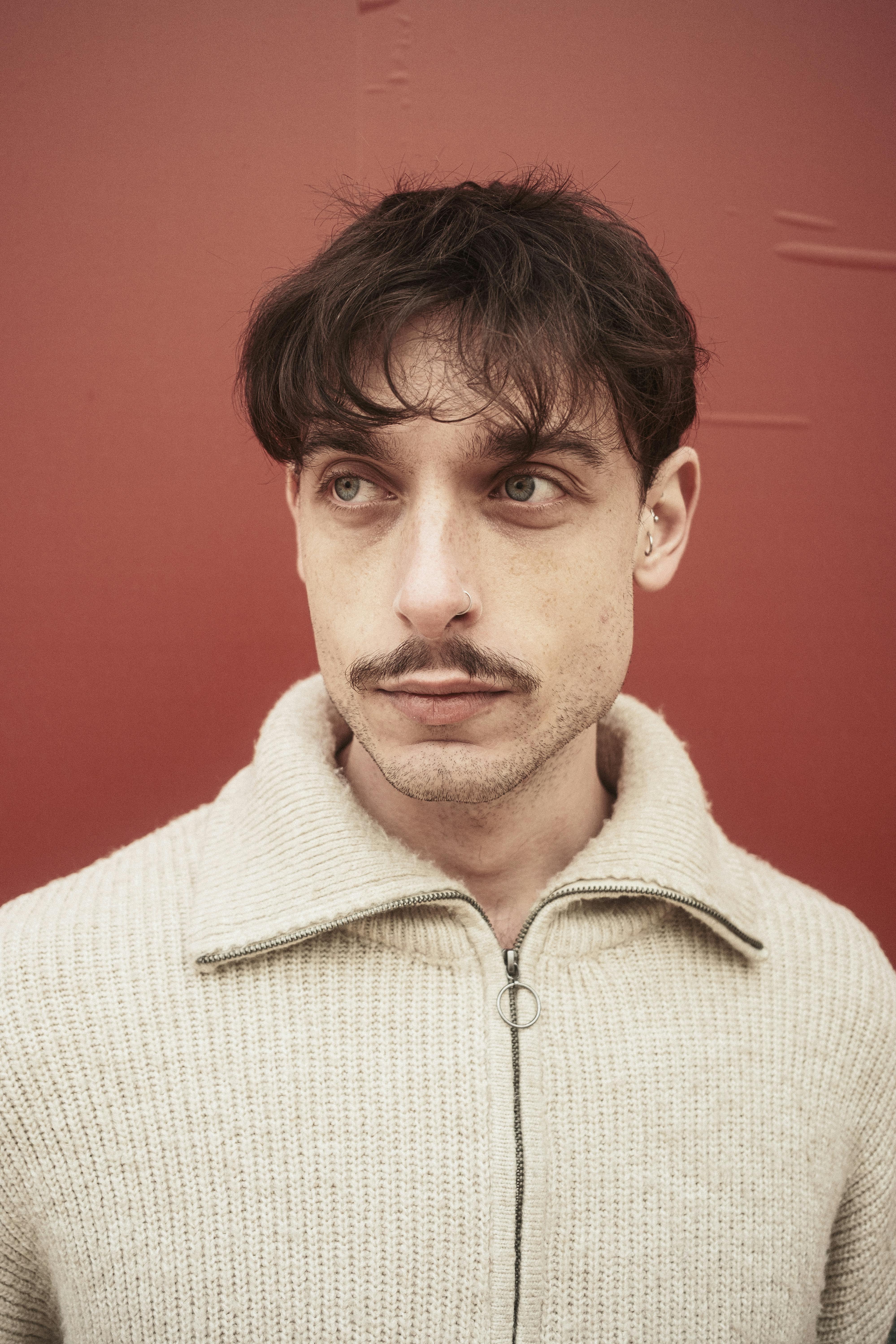 Close-up portrait of a man against a red wall, capturing a contemplative mood.