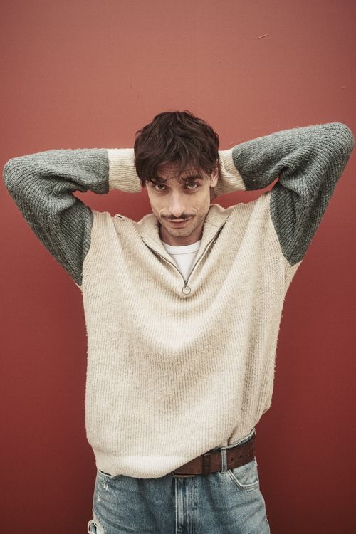 Free Man in a sweater and jeans posing with hands behind head against red wall. Stock Photo