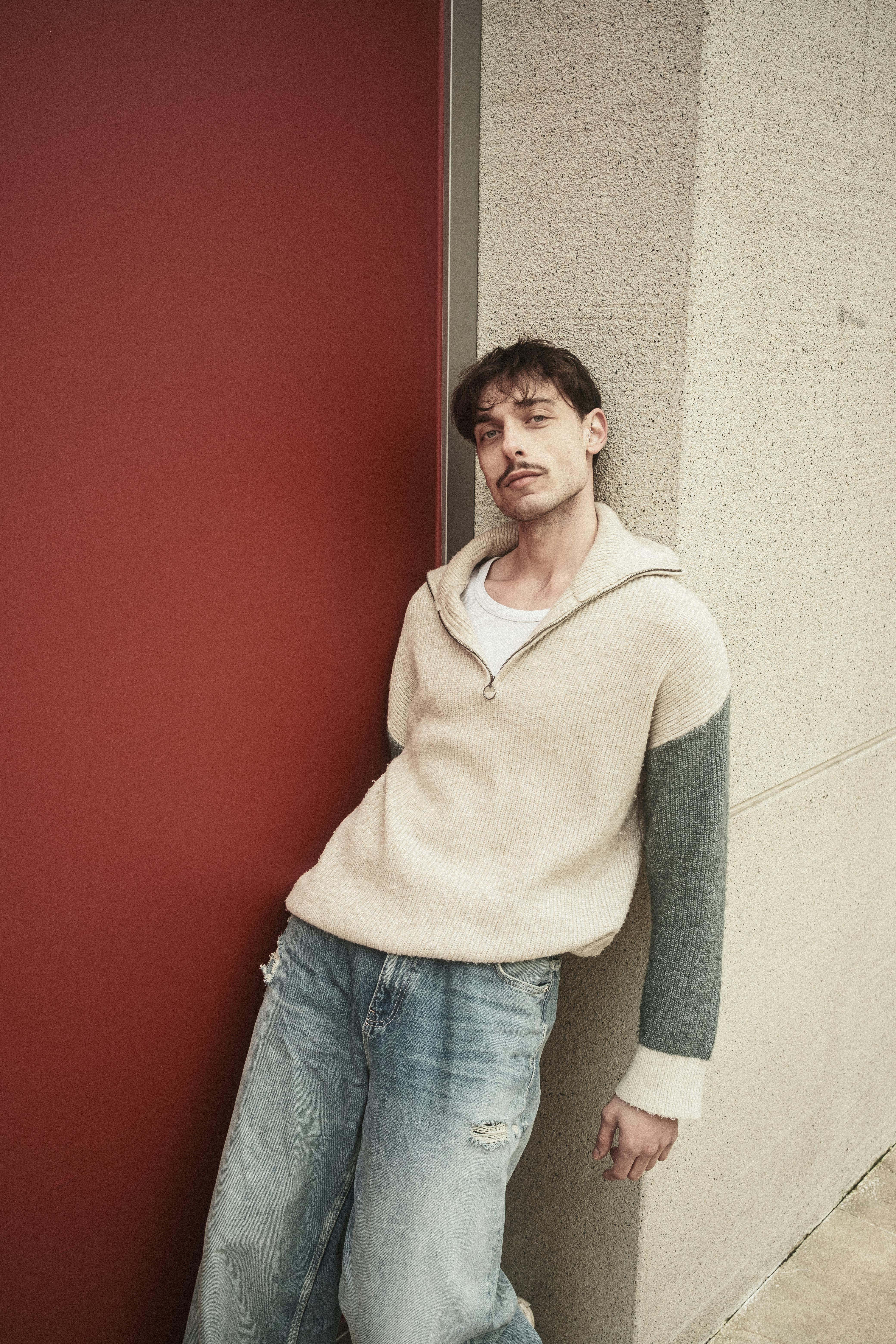 Bezpłatne Stylowy młody mężczyzna w swobodnym stroju opiera się o czerwoną ścianę na świeżym powietrzu. Zdjęcie z galerii