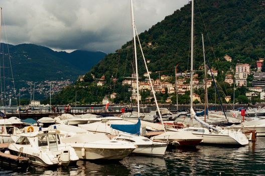 A picturesque view of boats docked in the Marina of Como, Italy with lush green hills in the background.