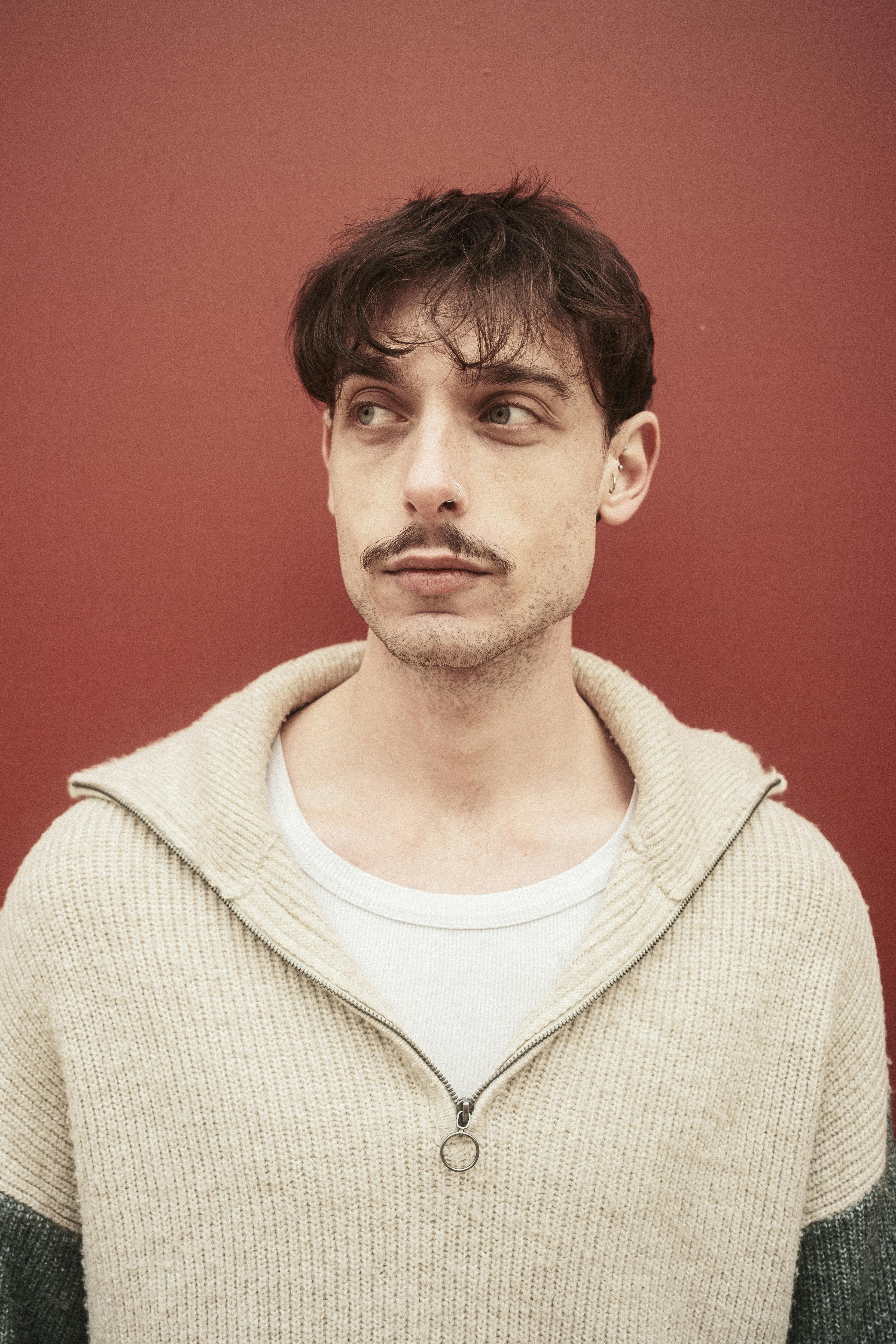 Portrait of a young man in a casual sweater against a red background, gazing thoughtfully.