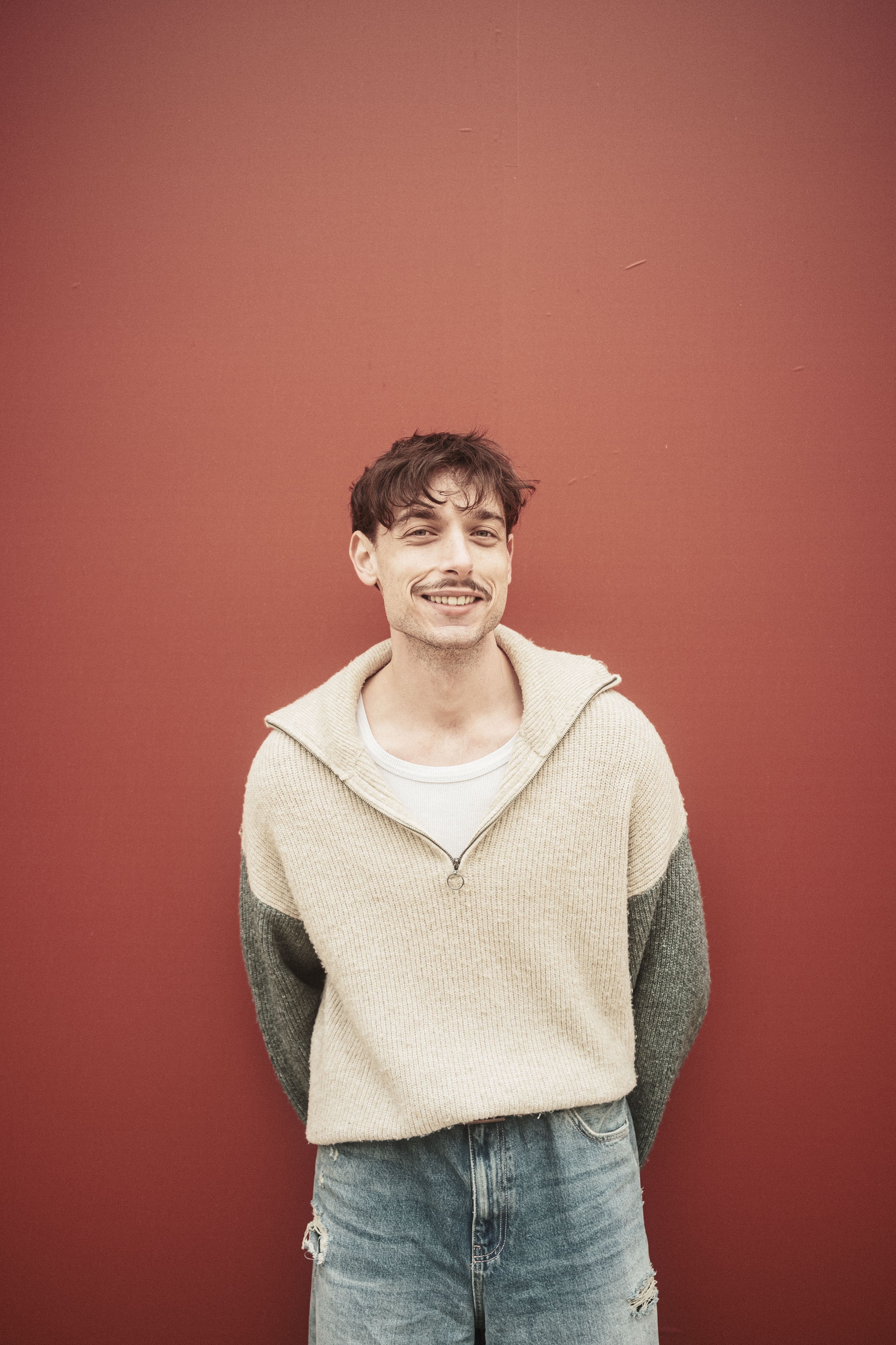 Casual portrait of a young man smiling in front of a red wall, exuding a relaxed and cheerful vibe.