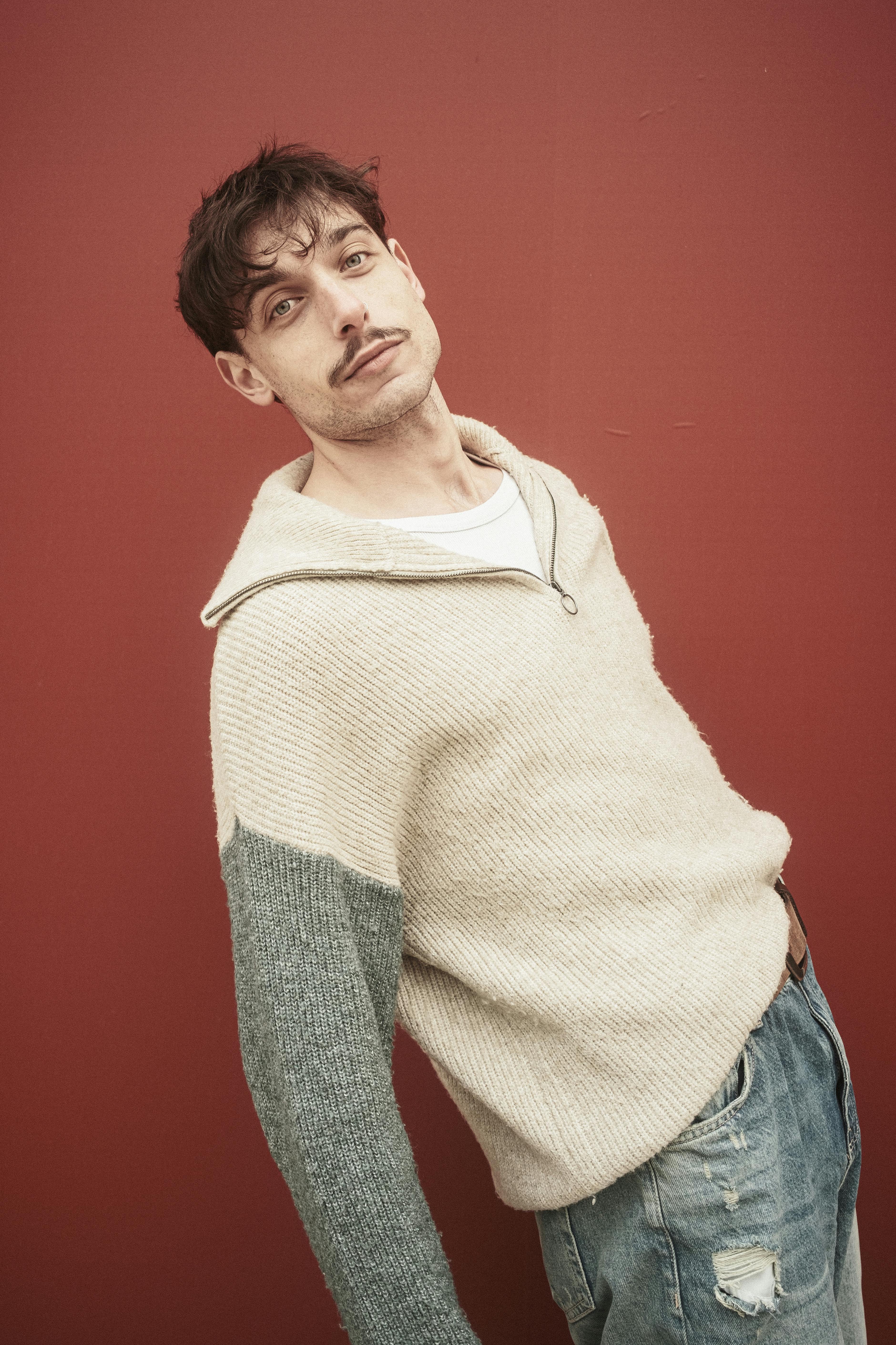 Portrait of a young man in a casual sweater against a red wall.