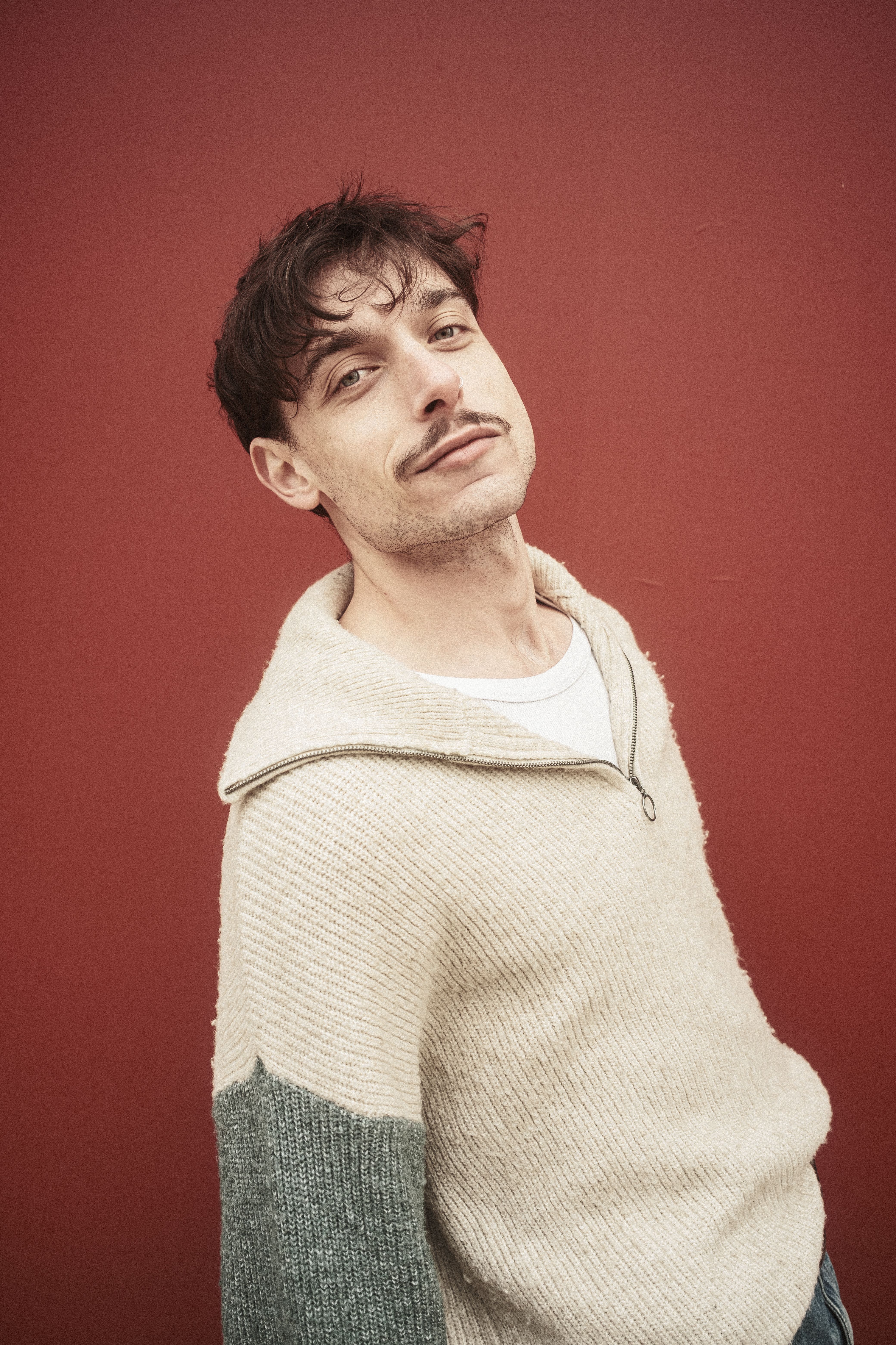 Portrait of a relaxed man wearing a sweater against a red wall, exuding a casual vibe.