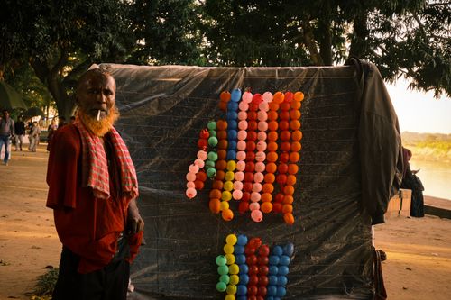 Free An elderly man stands beside a wall of colorful balloons outdoors. Stock Photo