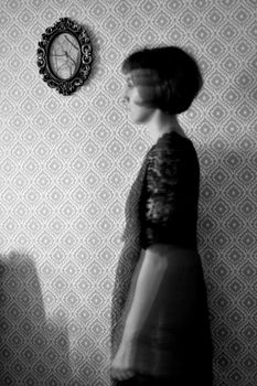 Artistic black and white image of a blurred woman against a vintage patterned wall.