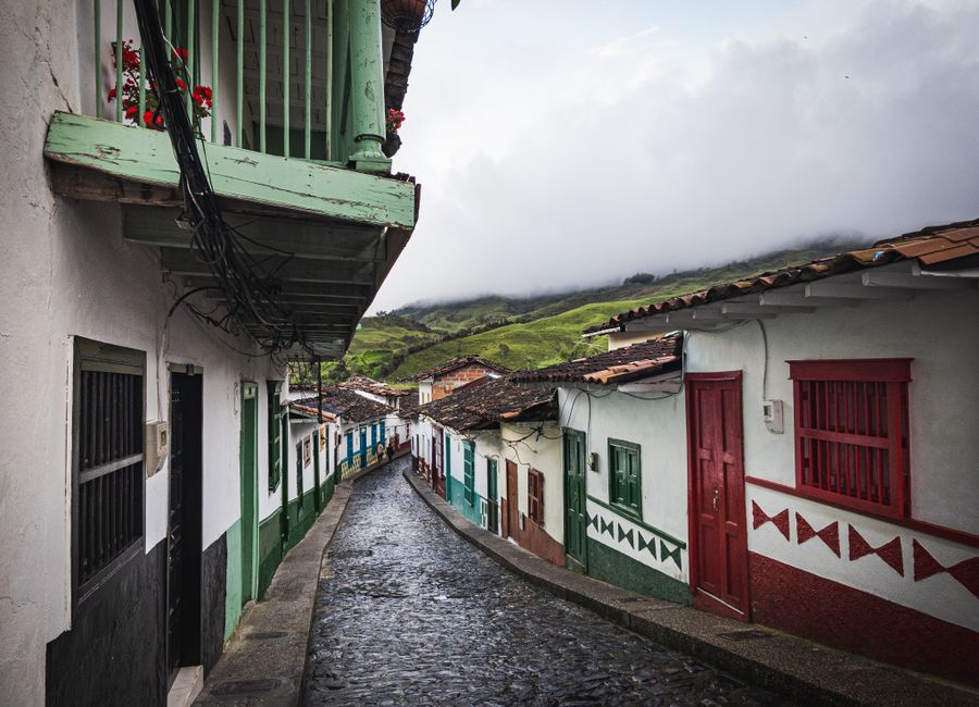 Charming cobblestone street lined with colorful houses in a Colombian village with lush green mountains.