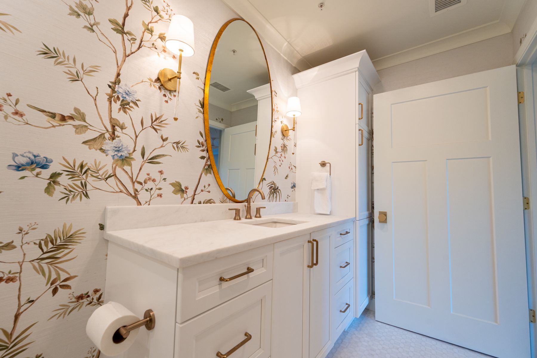 Bright shabby chic-inspired bathroom with floral wallpaper, white cabinetry and soft gold details