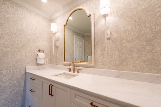 Luxurious bathroom vanity featuring marble countertop, gold fixtures, and decorative wallpaper.