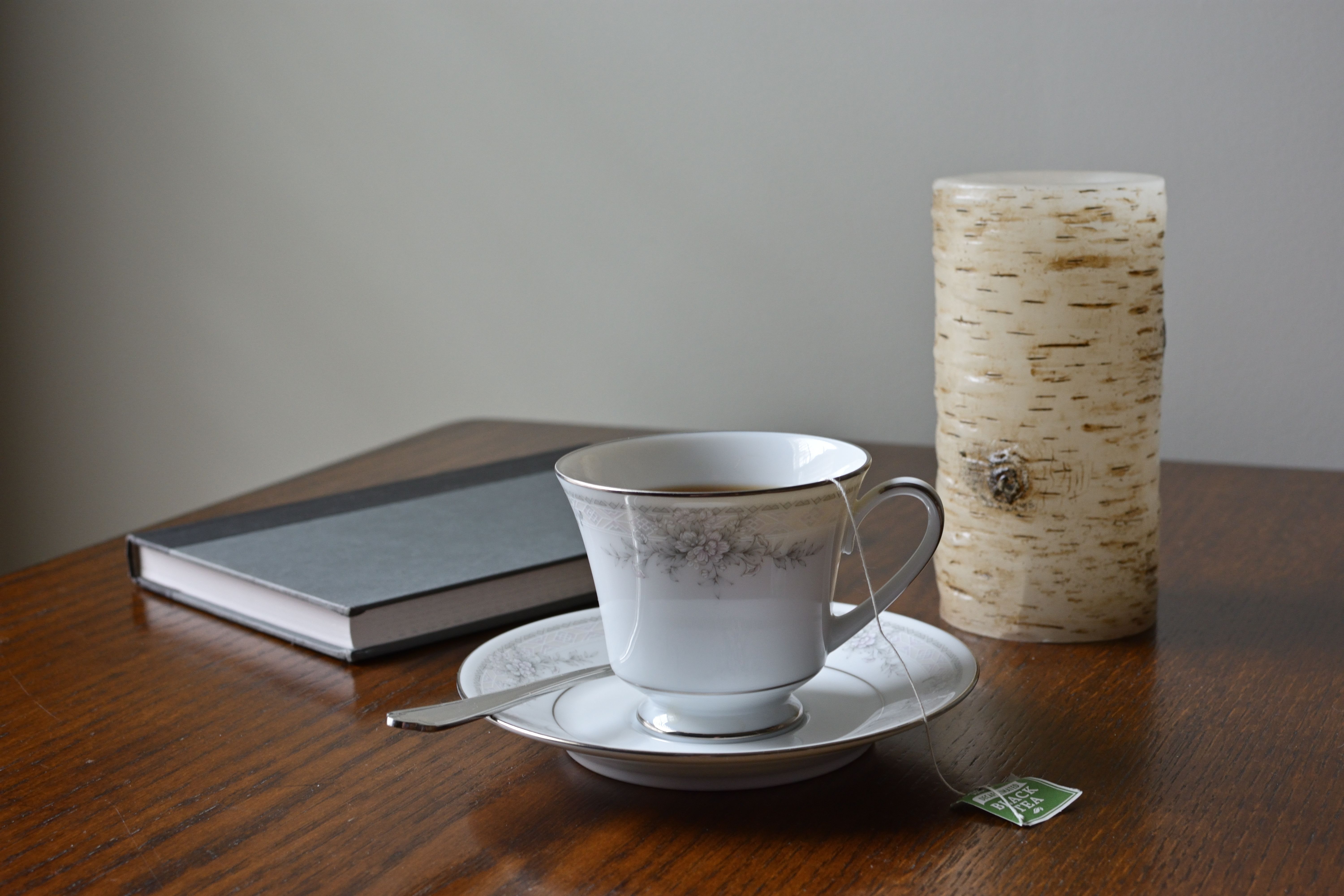 Elegant still life with a teacup, birch candle, and book on a wooden table.
