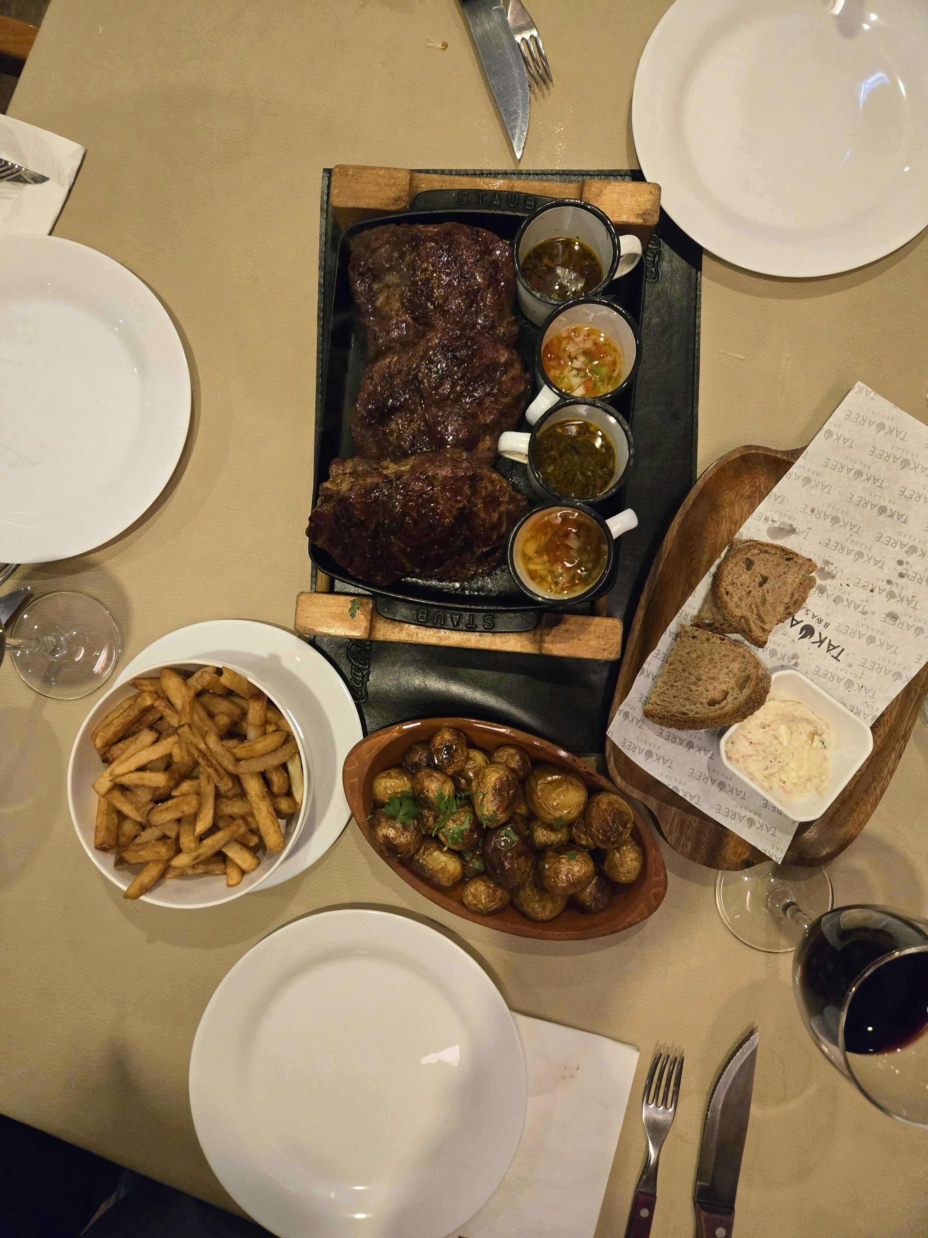Overhead view of a steak meal with fries, potatoes, bread, and sauces.