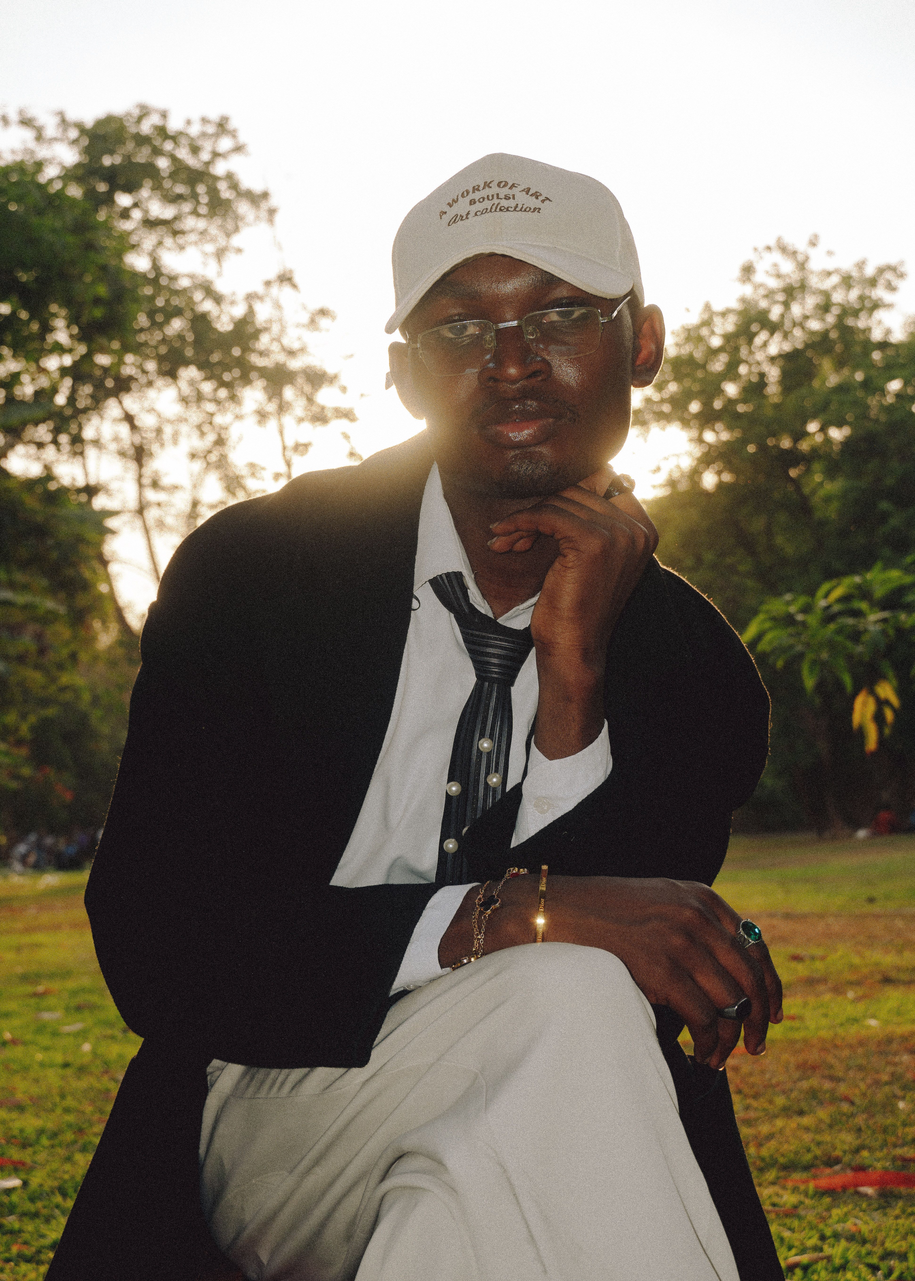 A fashionable man poses outdoors in the evening light, wearing a suit and hat, exuding elegance.
