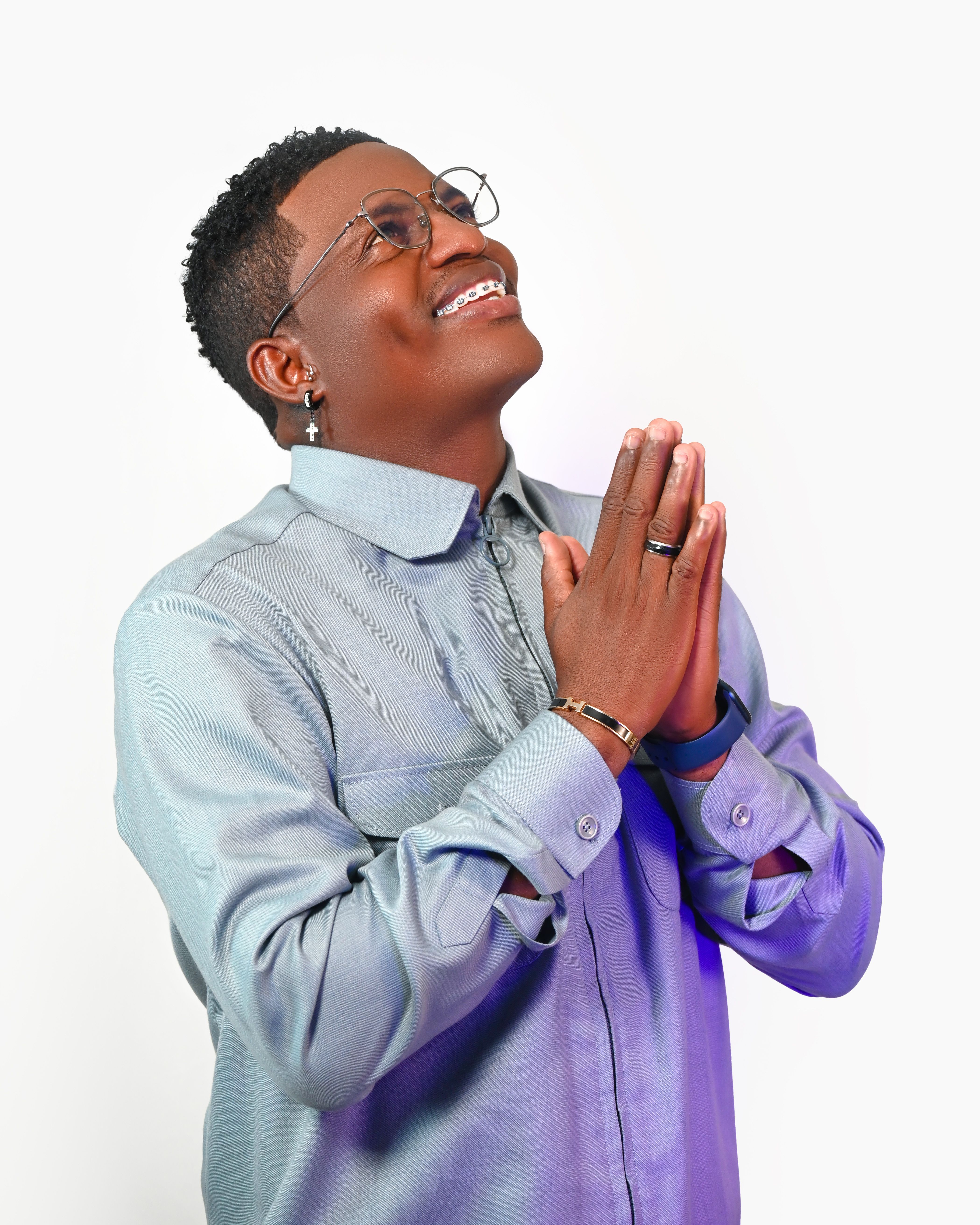 A smiling adult man in a light shirt praying with hands clasped, expressing gratitude and positivity.