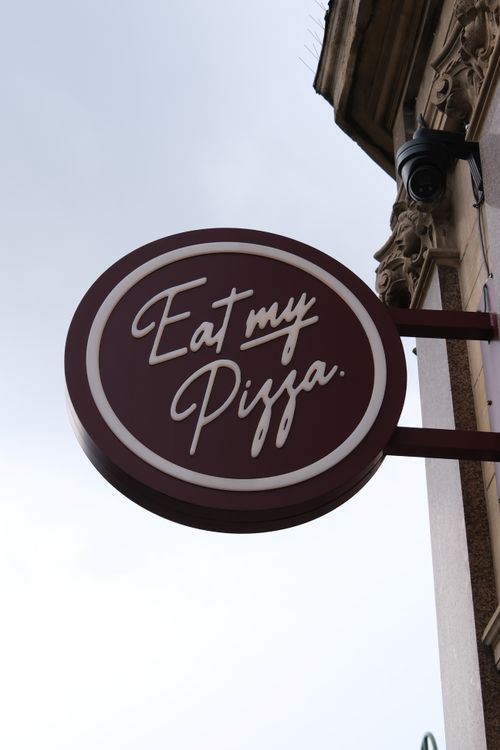 Free Red circular sign reading 'Eat my Pizza' on a London street. Perfect for urban dining themes. Stock Photo