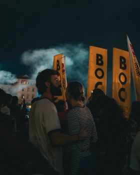 Crowded festival scene at night with illuminated flags and silhouetted people.