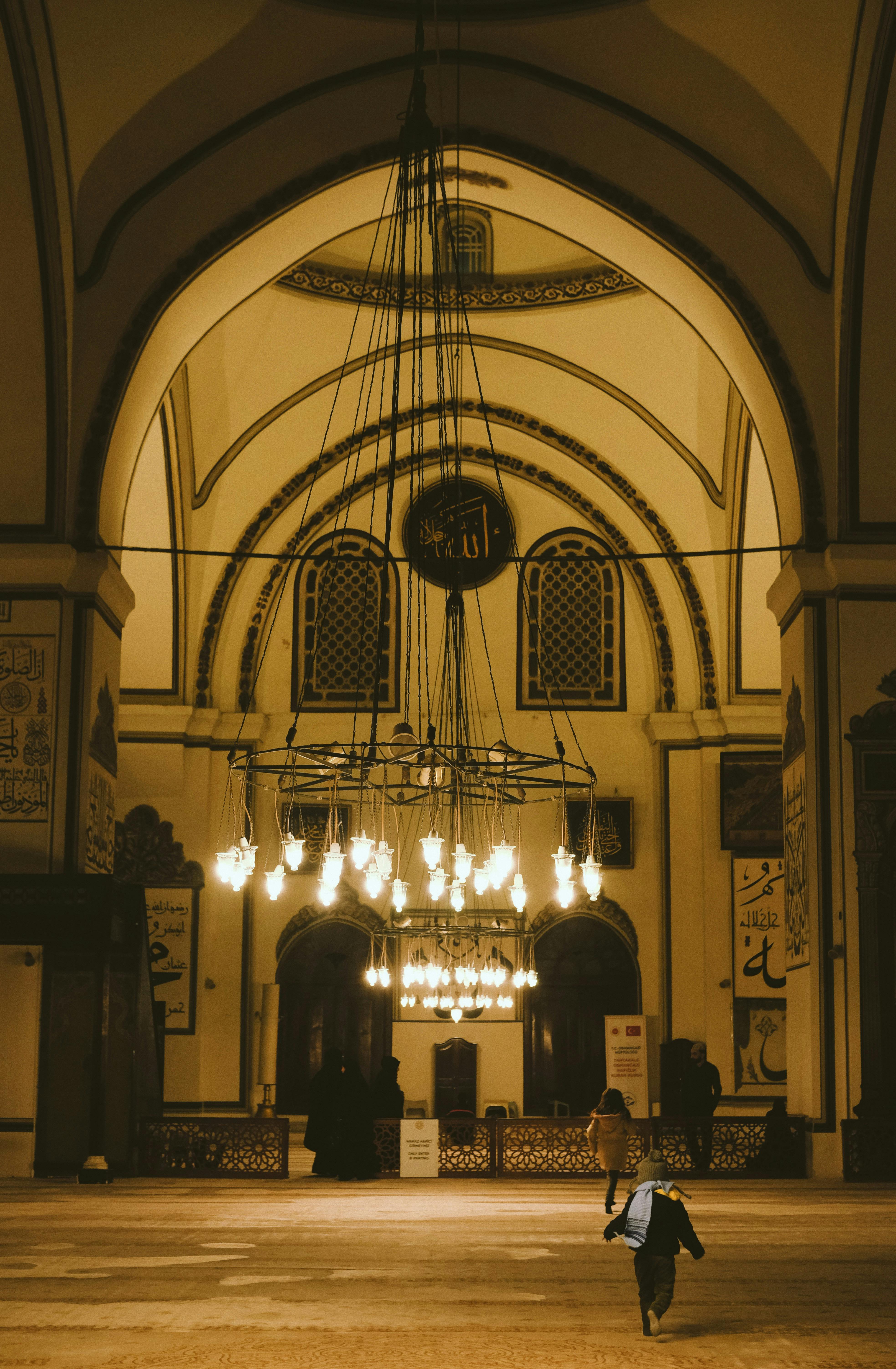 grátis Uma criança caminha à noite pelo interior de uma mesquita histórica lindamente iluminada, que exibe sua arquitetura intrincada. Foto profissional