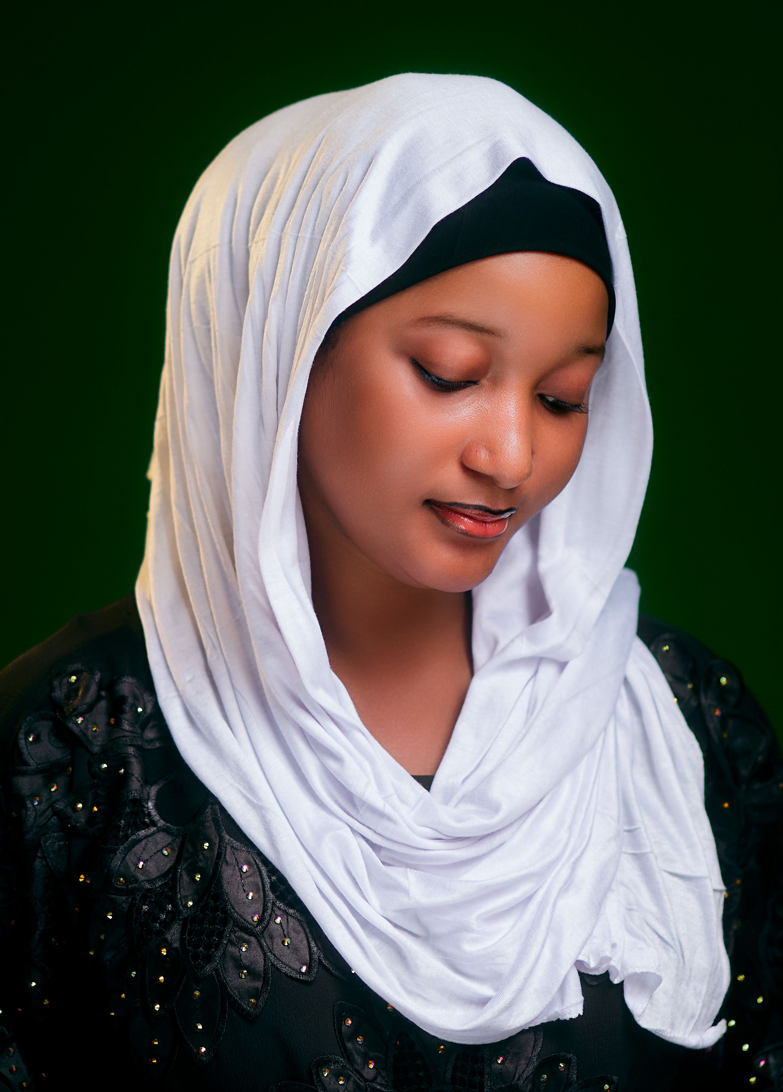 Elegant portrait of a woman in a white hijab, serene expression, dark contrasting background.