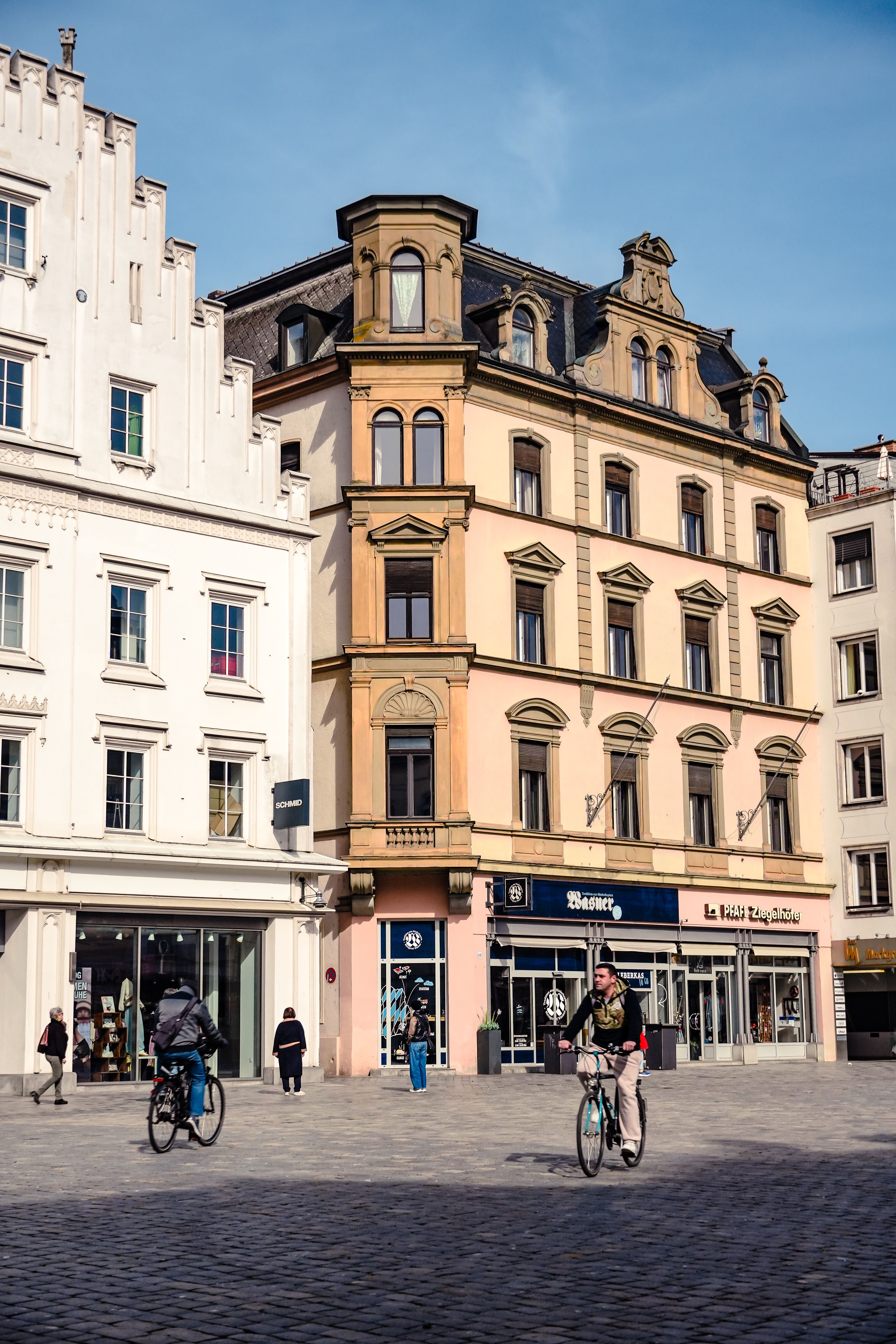 Cyclists pass by historic buildings in a German city square, showcasing classic architecture.