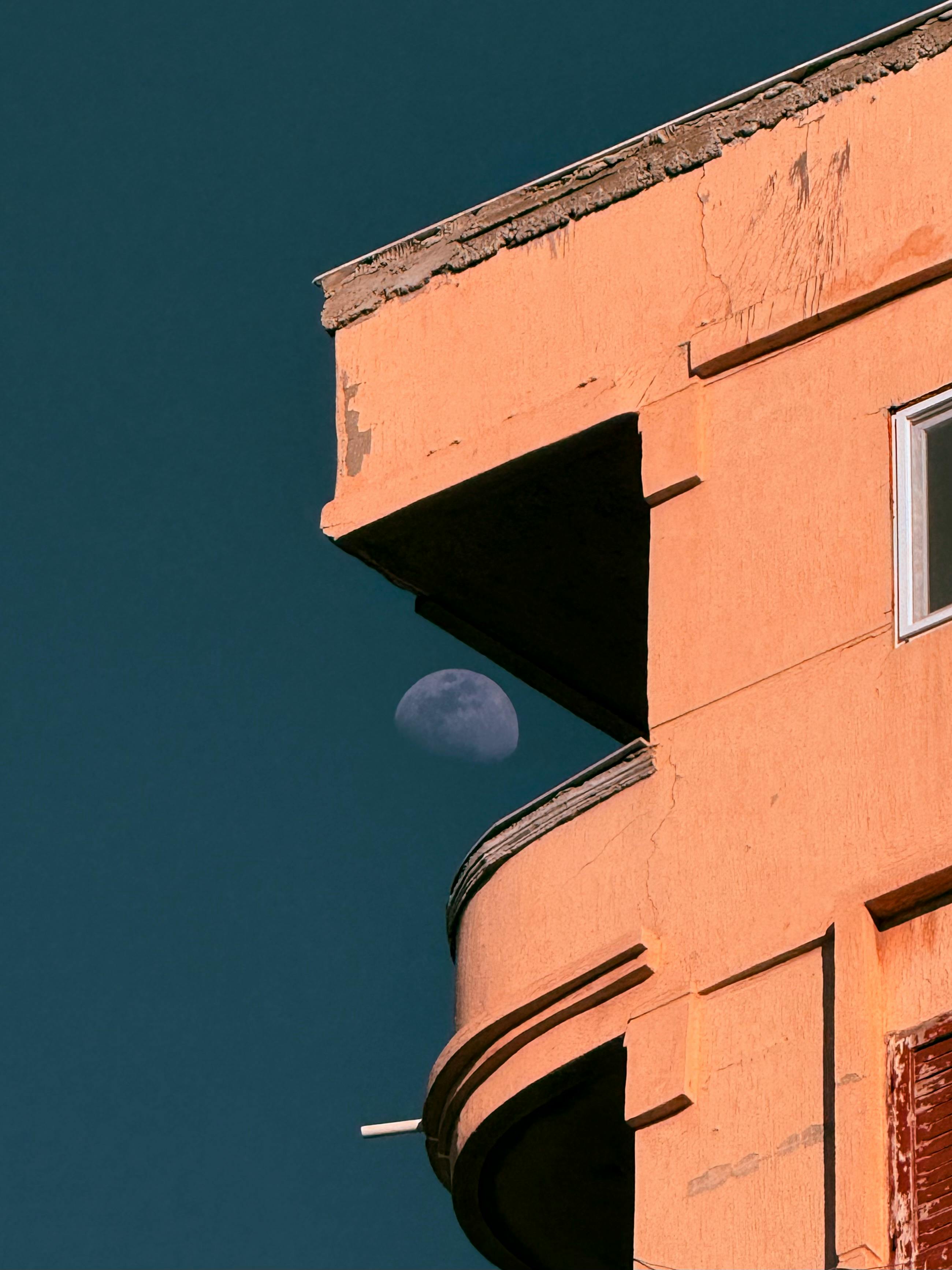 grátis Vista da lua espreitando por trás de um prédio em Alexandria, Egito, capturada em impressionante contraste com o céu profundo. Foto profissional