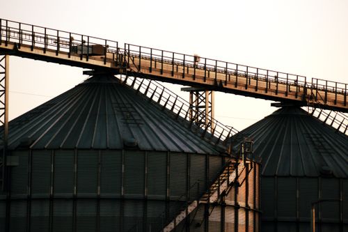 Free Close-up image of industrial grain silos with overhead walkway at sunset, conveying modern industry. Stock Photo